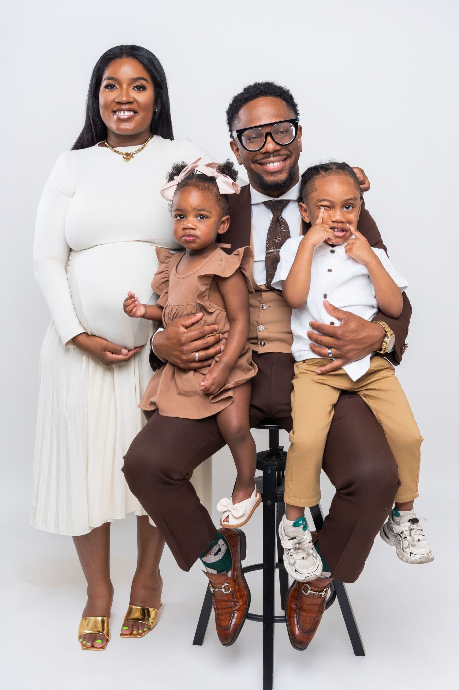 Family in coordinated brown and white outfits pose together in studio against white backdrop for professional photos.
