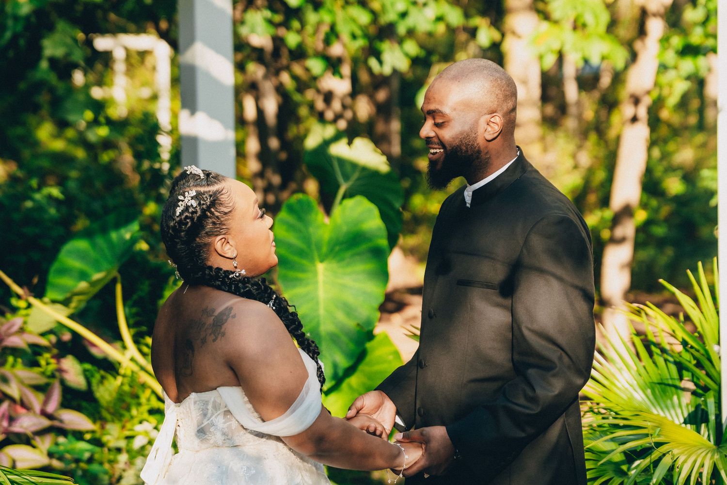 A couple shares an intimate moment during their outdoor wedding ceremony surrounded by lush tropical greenery.