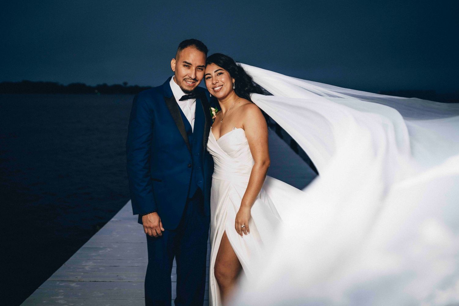 A wedding couple shares an intimate joyful moment together while the bride's veil flows in the wind.