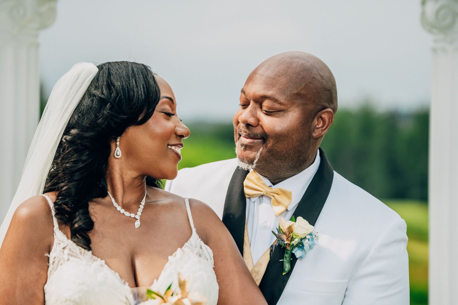A joyful couple shares a candid moment together on their wedding day, wearing a white dress and tuxedo with gold bow tie.