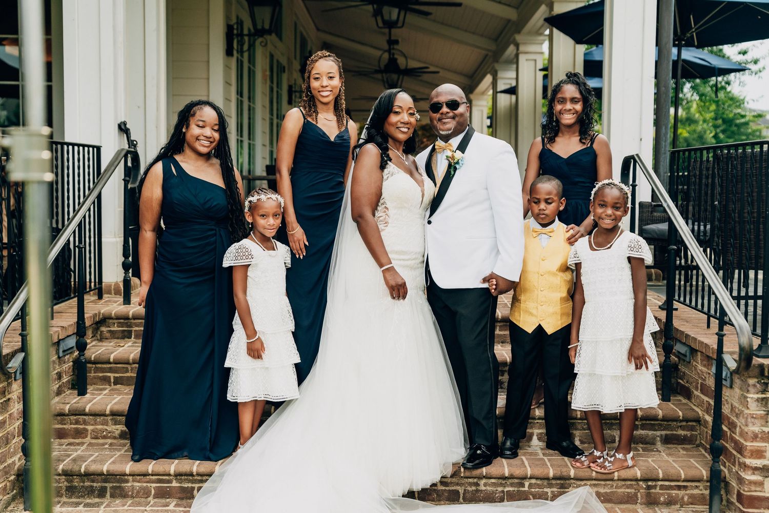 A wedding party poses outdoors in formal attire with bridesmaids in white dresses and black dresses.