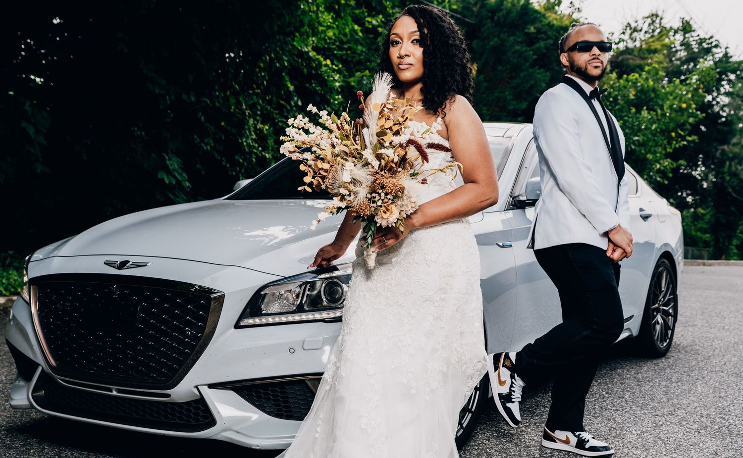 Luxury silver Genesis vehicle parked on asphalt with a white wedding dress visible in the frame.