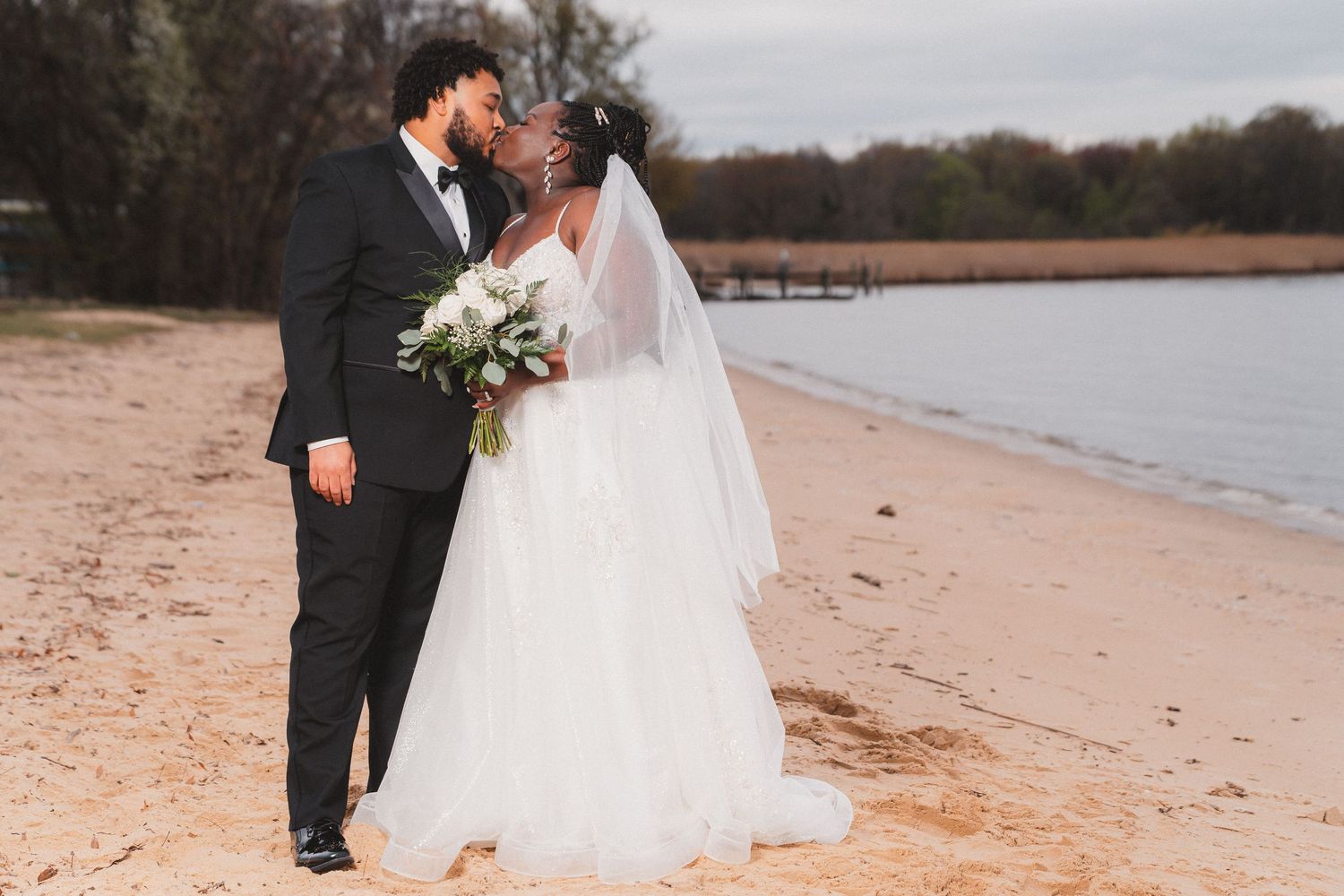 A couple shares romantic moments on a sandy beach during their wedding photo session at sunset.