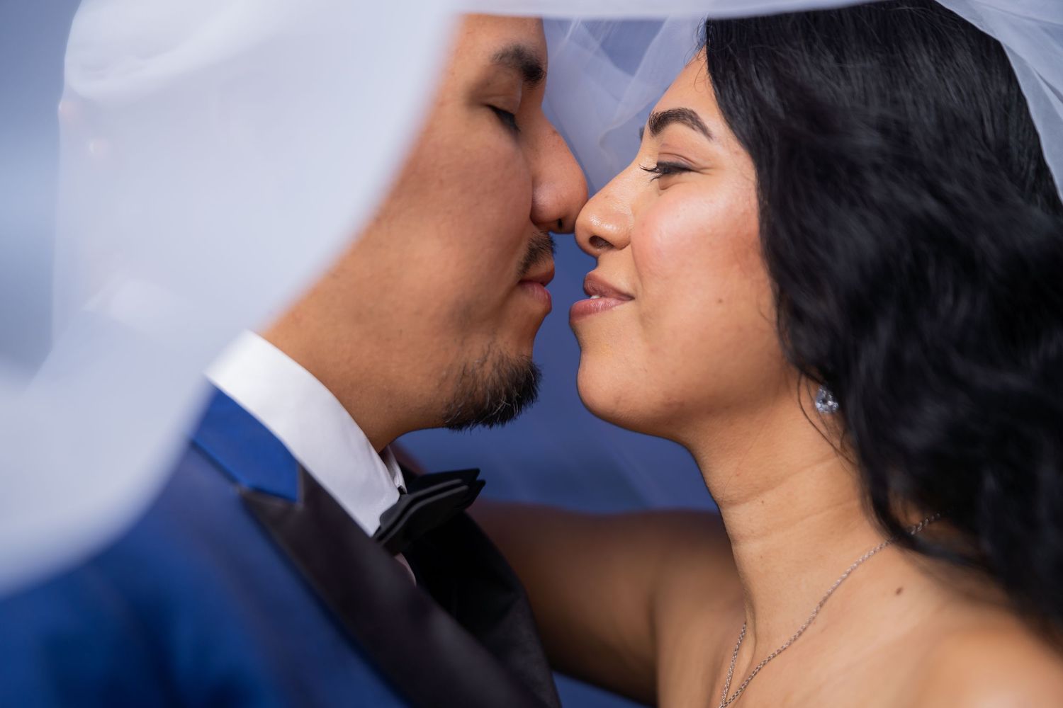 A couple in wedding attire share an intimate moment against a soft blue background.