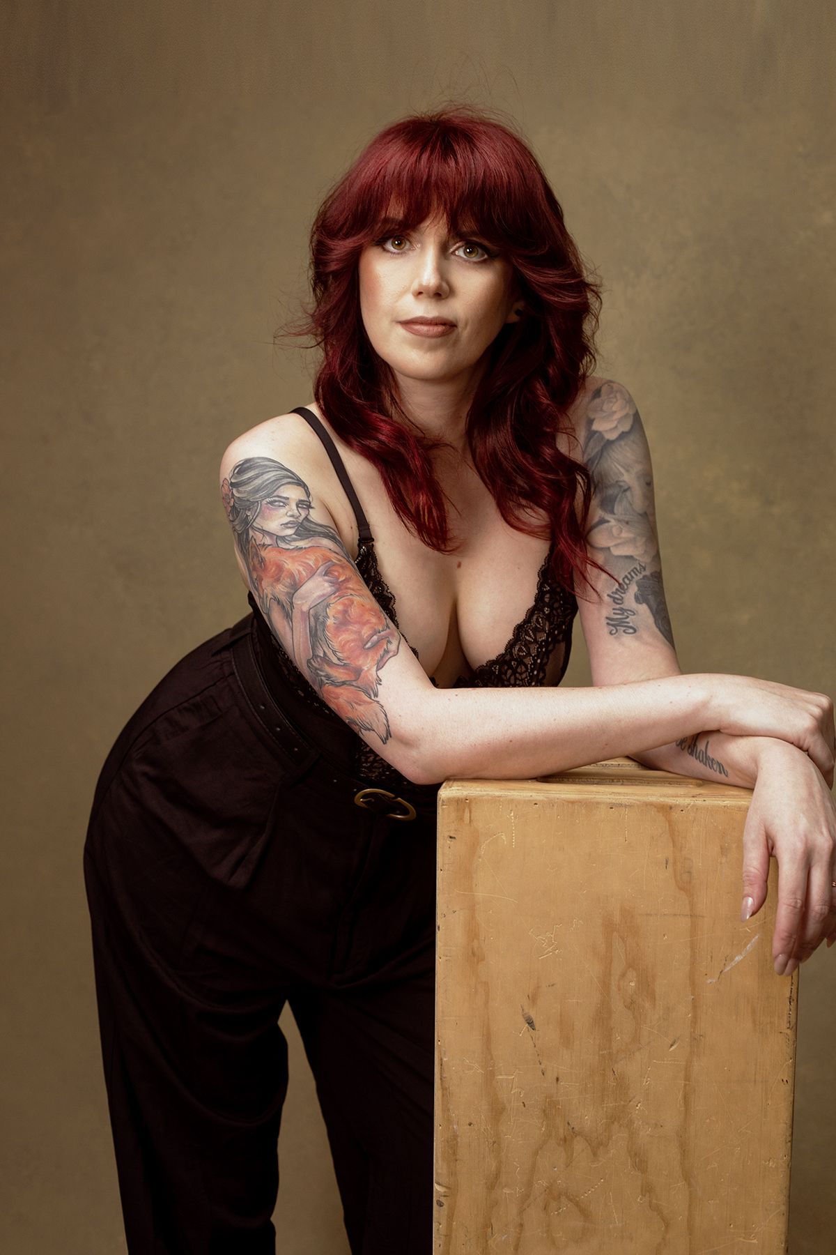 Studio portraits featuring tattooed arms and black outfit posed with wooden box prop.