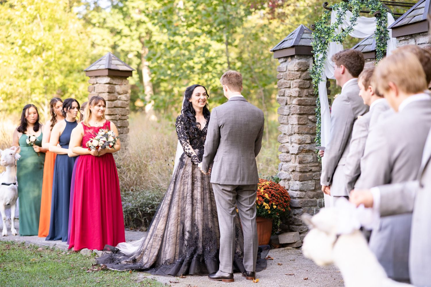 Bride in black lace gown exchanges vows with groom at outdoor stone wedding ceremony.