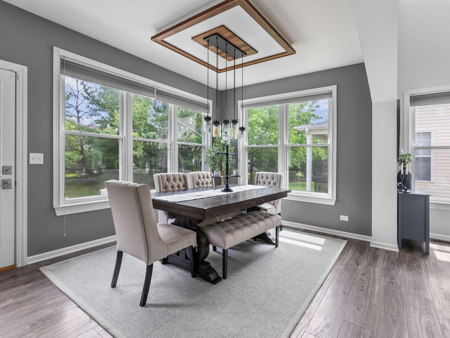 Modern dining room with large windows, gray walls, wood floors, and contemporary chandelier lighting fixture above table.