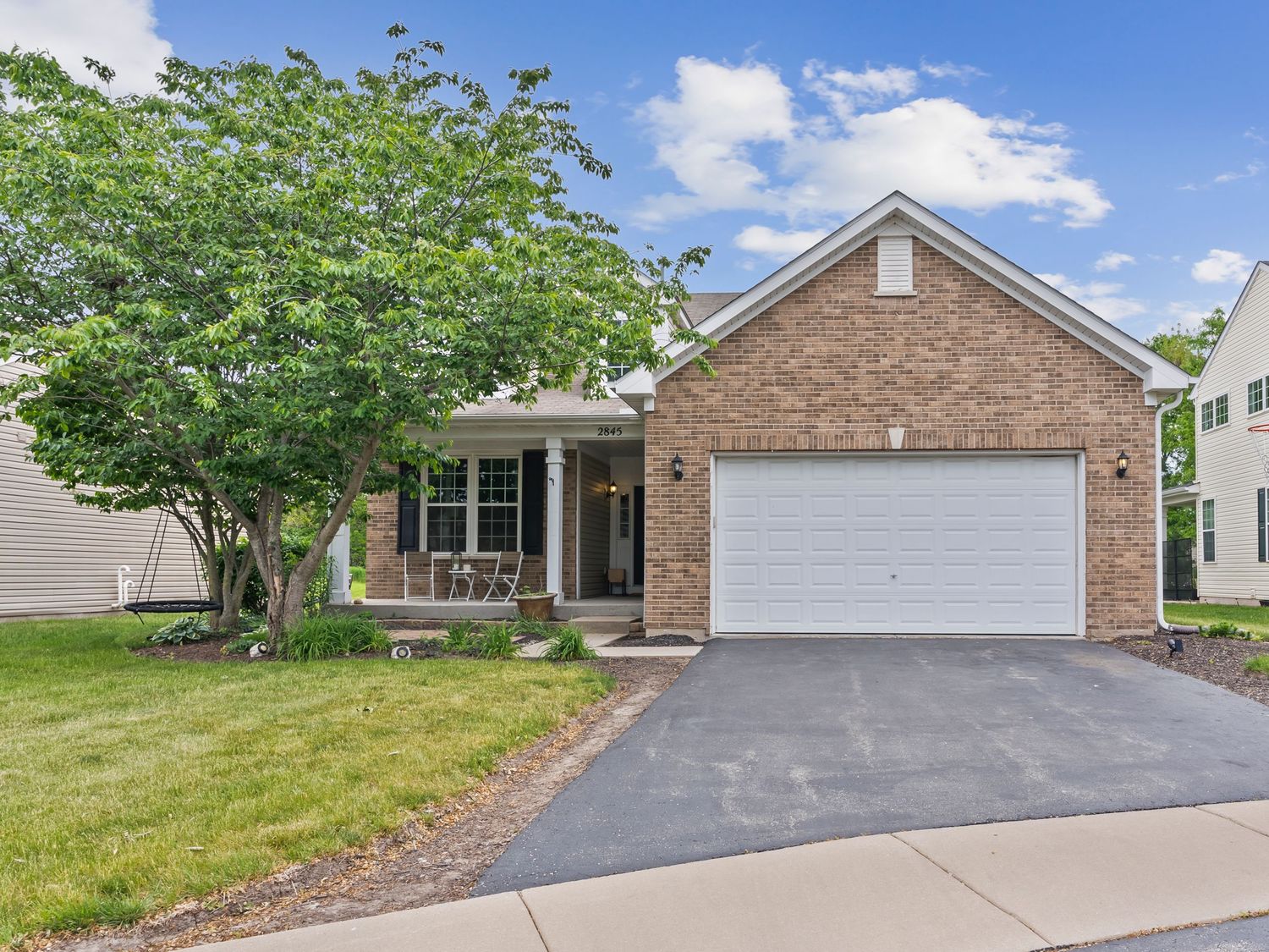 Single story brick ranch home with white garage door, green lawn and mature tree in suburban setting.