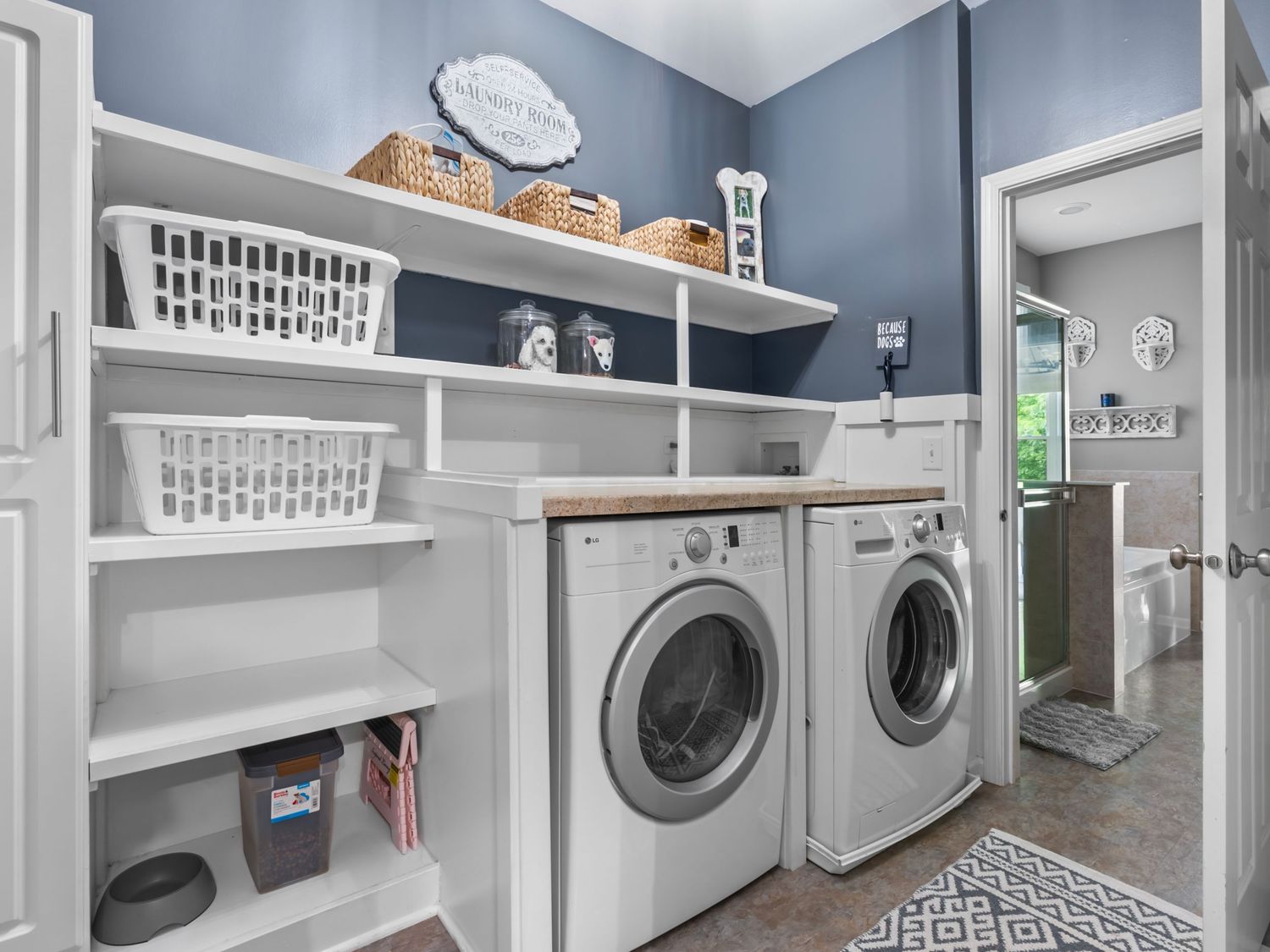 Modern laundry room with gray walls featuring white built-in shelving, storage baskets, and side-by-side washer dryer.