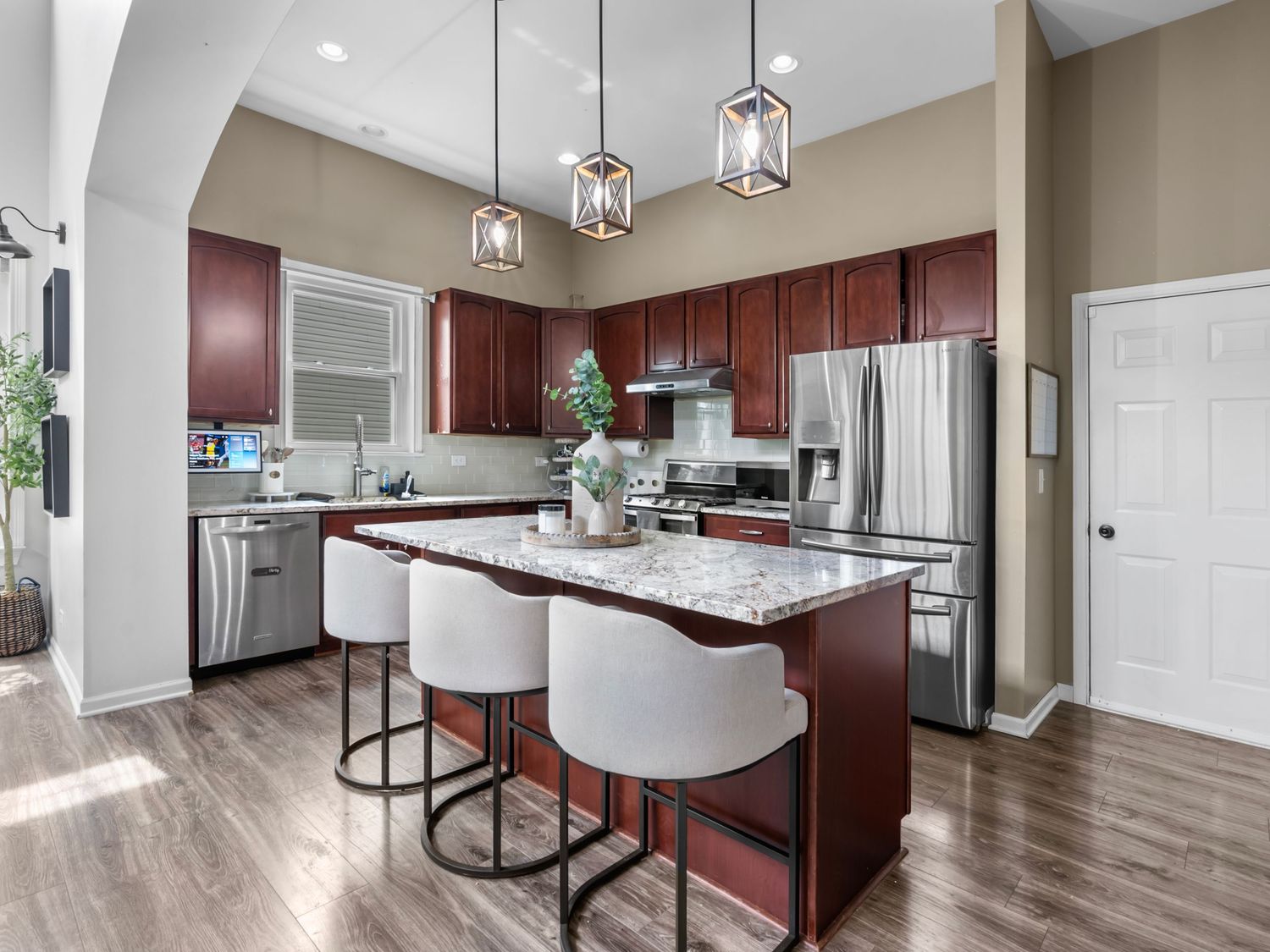 Modern kitchen featuring dark wood cabinets, white quartz countertops, and pendant lighting over a breakfast bar with white stools.