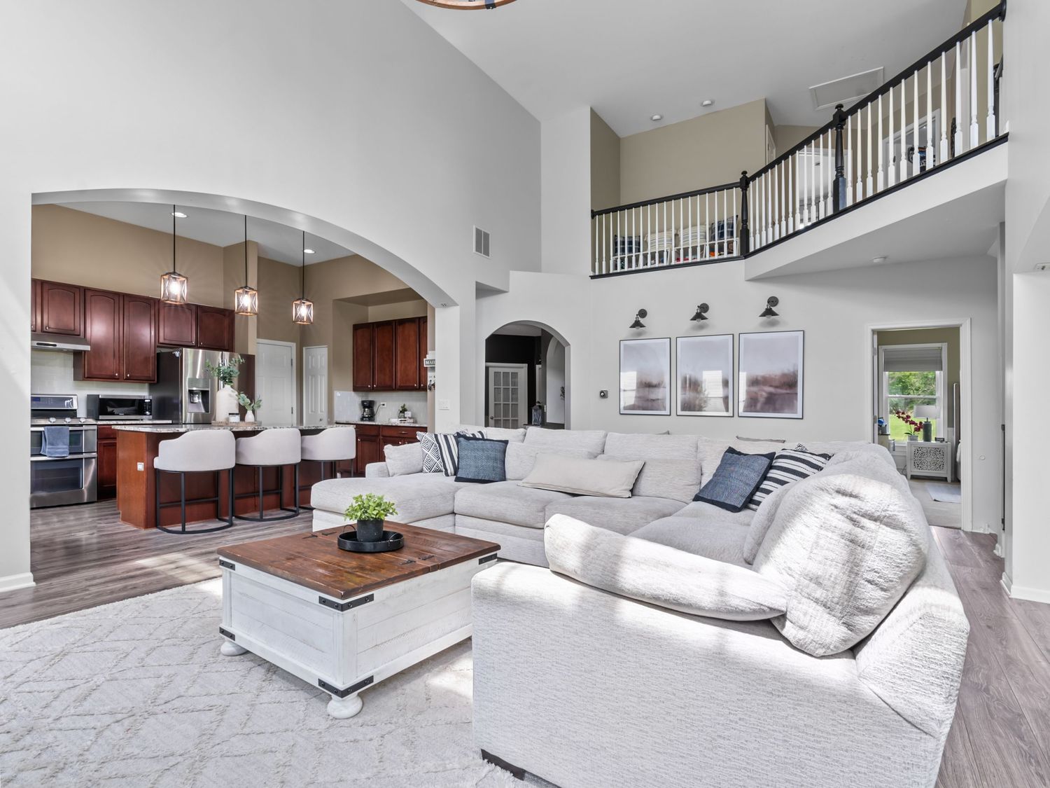 Luxurious open-concept living room with high ceilings, white sectional sofa, and modern kitchen visible in an elegant home.