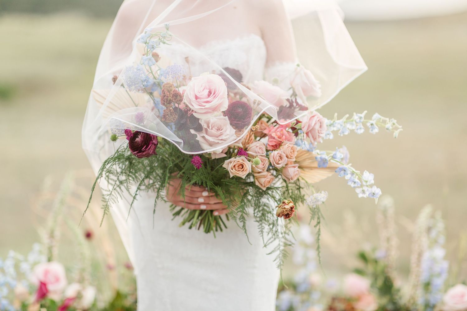 Elegant wedding bouquet with pink and white roses, delicate greenery, and trailing ribbons in a soft outdoor setting.