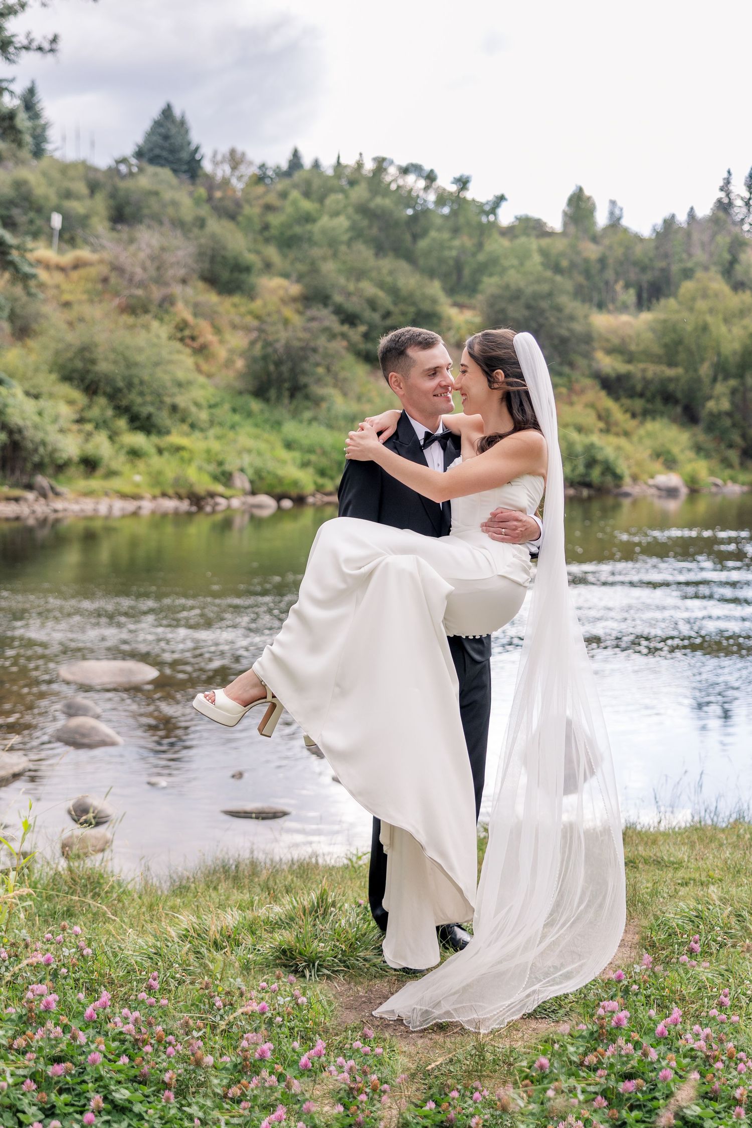 Romantic wedding photos by a serene riverside with flowing white dress and natural scenery.