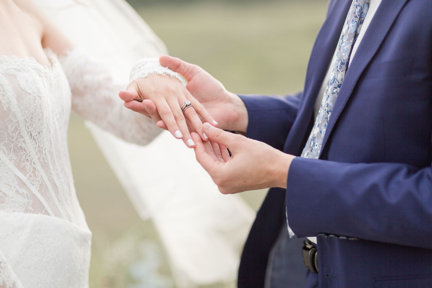 A tender moment during a wedding ceremony as a groom kisses the bride's hand outdoors.