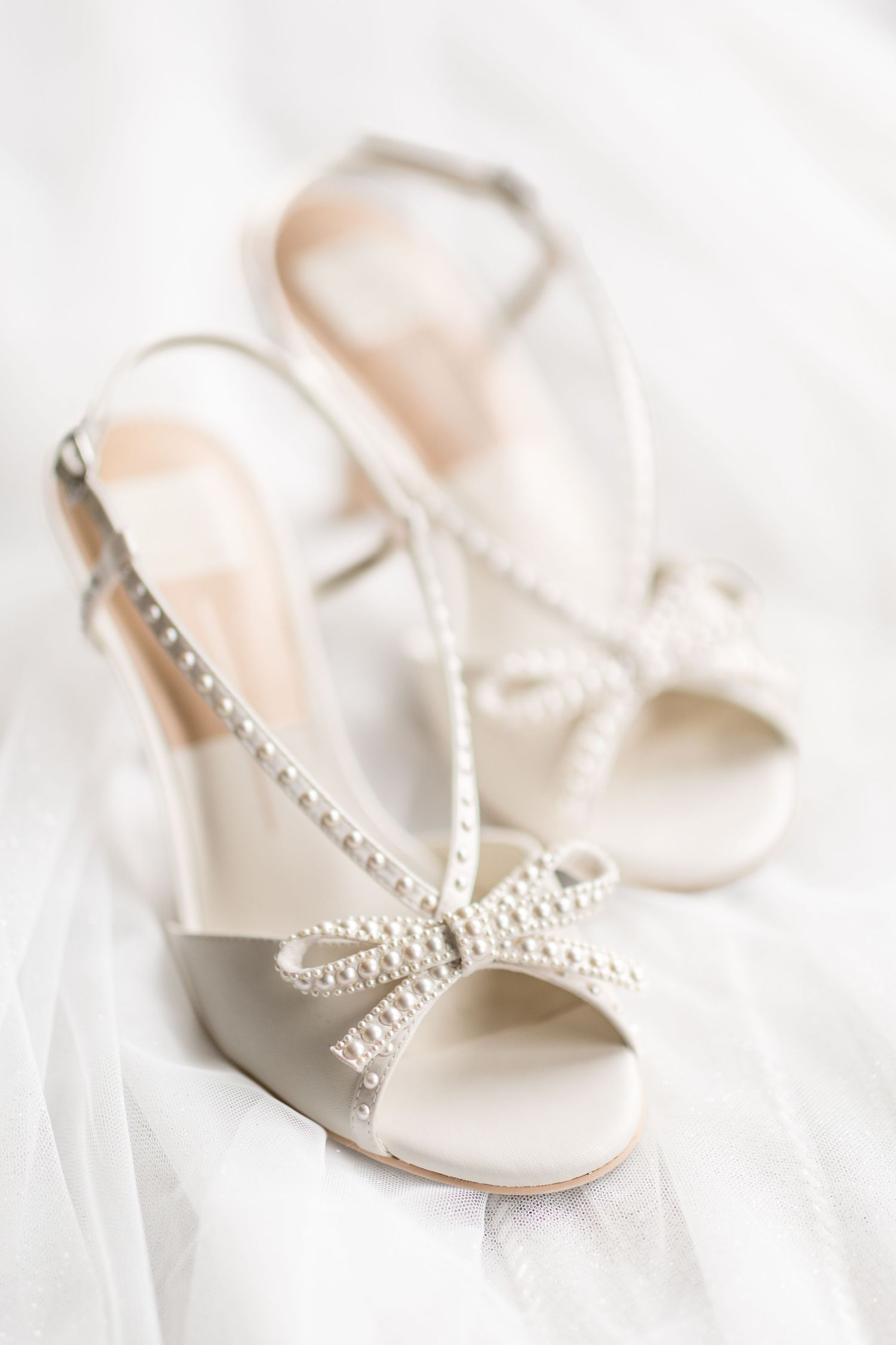 Elegant white bridal sandals with pearl embellishments and slingback straps displayed on soft white fabric.