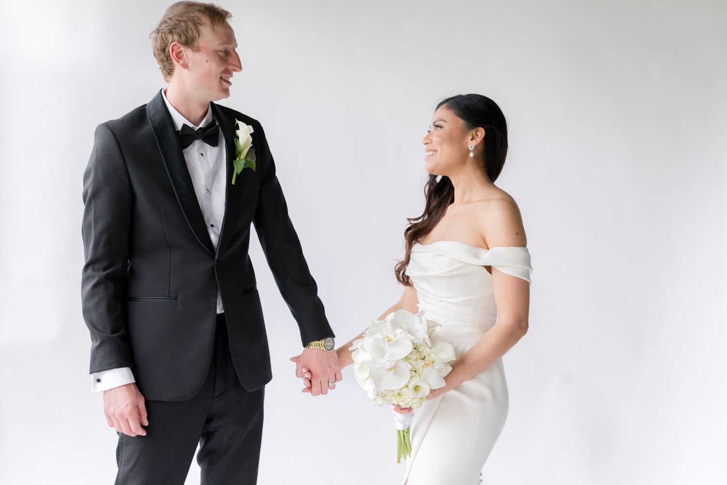 A wedding couple enjoying a light-hearted moment together against a white background.