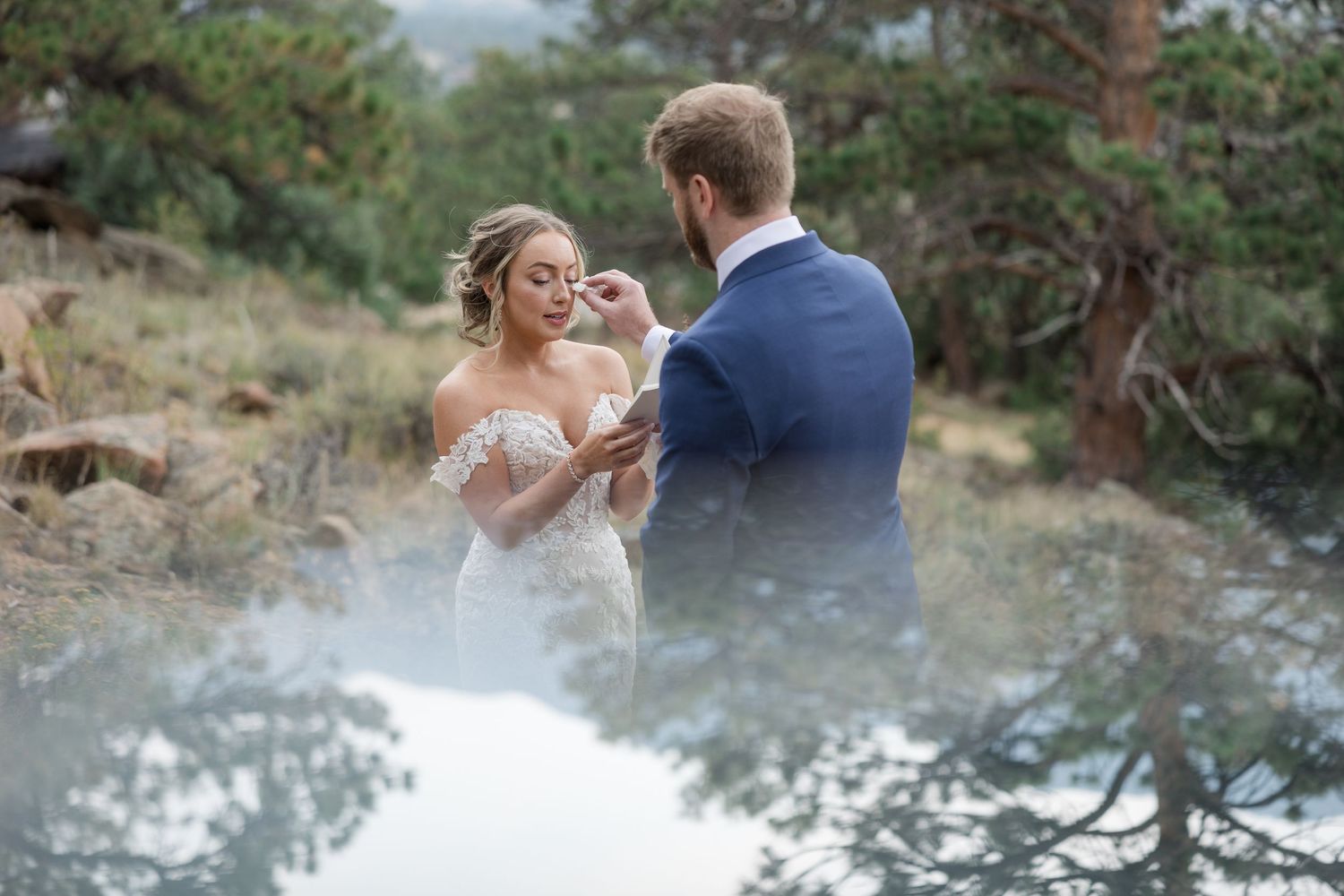 A couple shares a romantic moment in their wedding attire among pine trees on a misty mountainside.