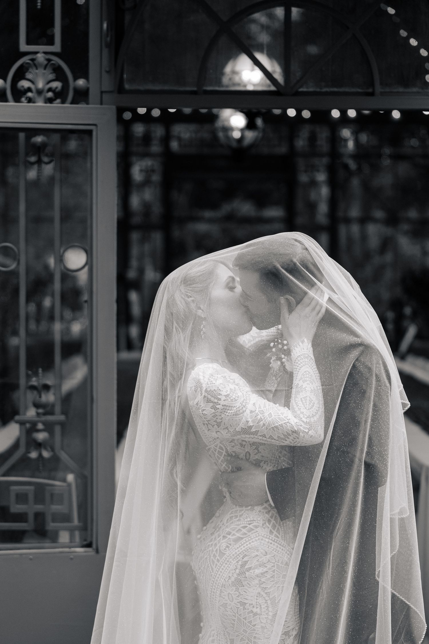 A close-up view of a delicate white lace wedding dress with sheer veil displayed in an elegant bridal boutique setting.