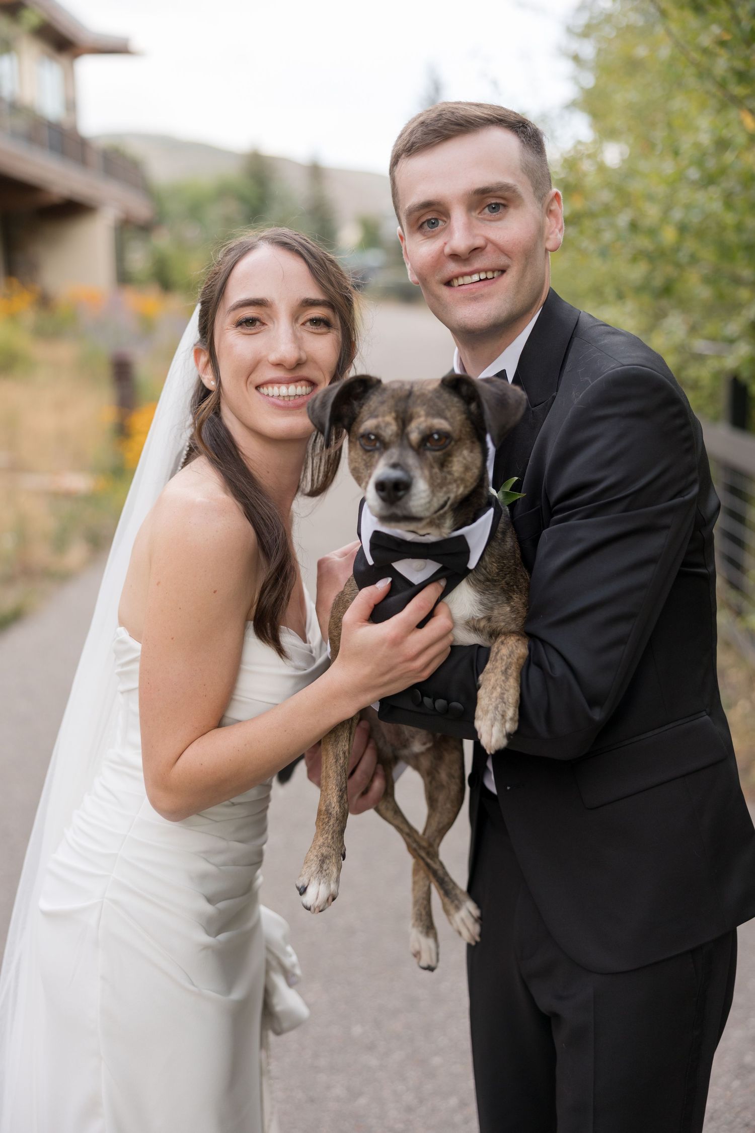 Wedding couple poses with their beloved brown dog in outdoor autumn setting.