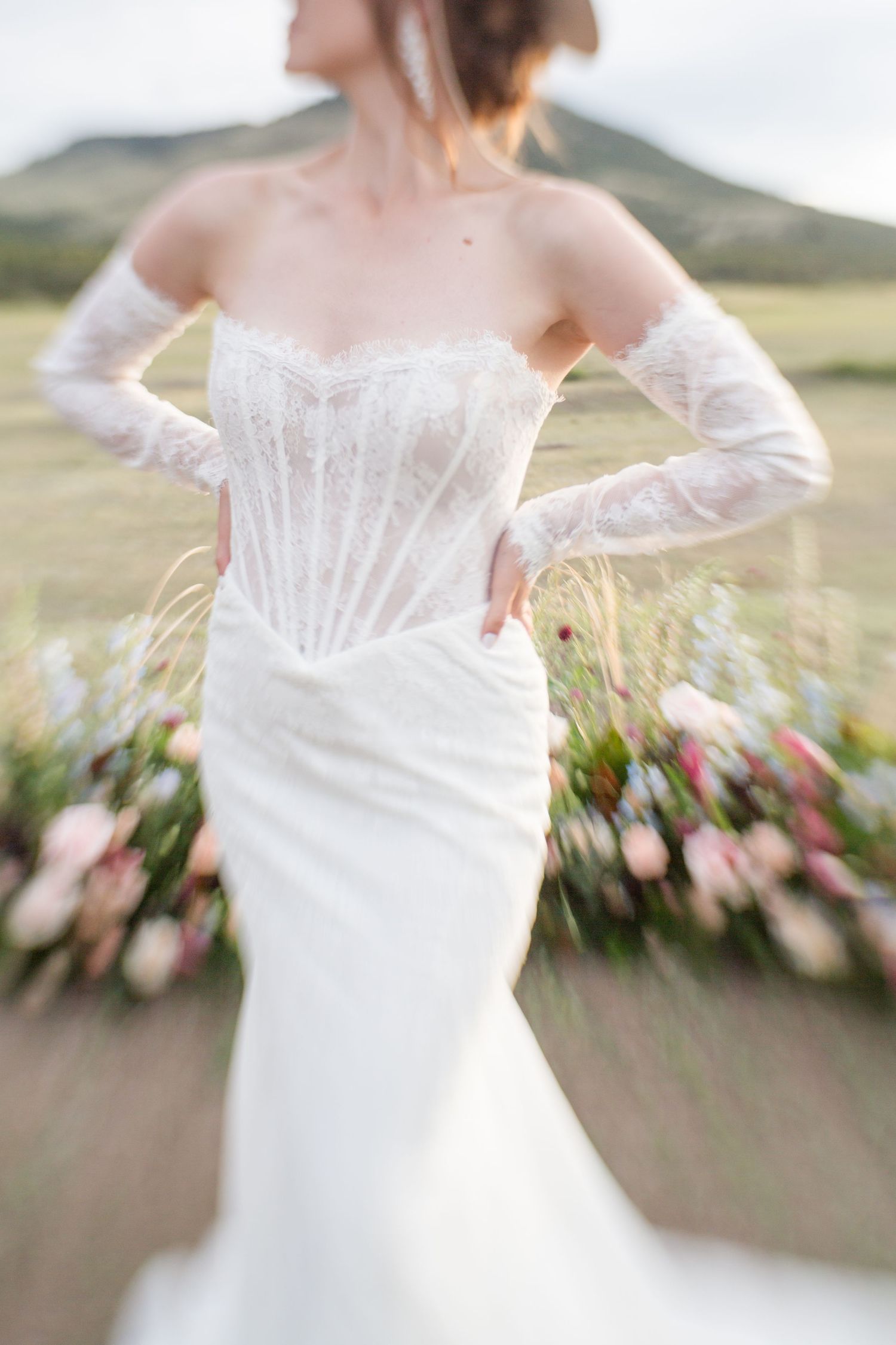 A close-up view of a white wedding dress bodice with delicate lace details and off-shoulder design against a blurred background.