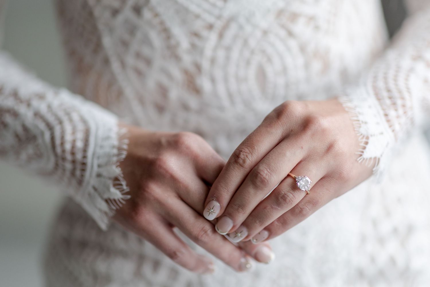 Close up details of hands wearing delicate lace sleeves and elegant engagement ring.