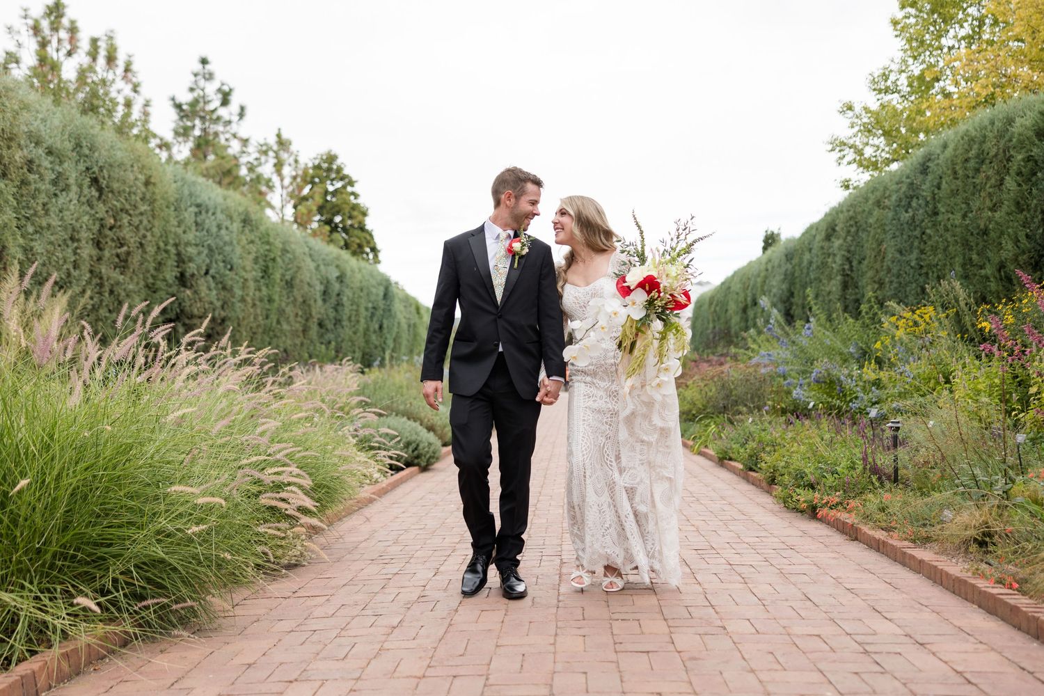 Couple walking together on a brick path surrounded by lush gardens and greenery during an outdoor celebration.