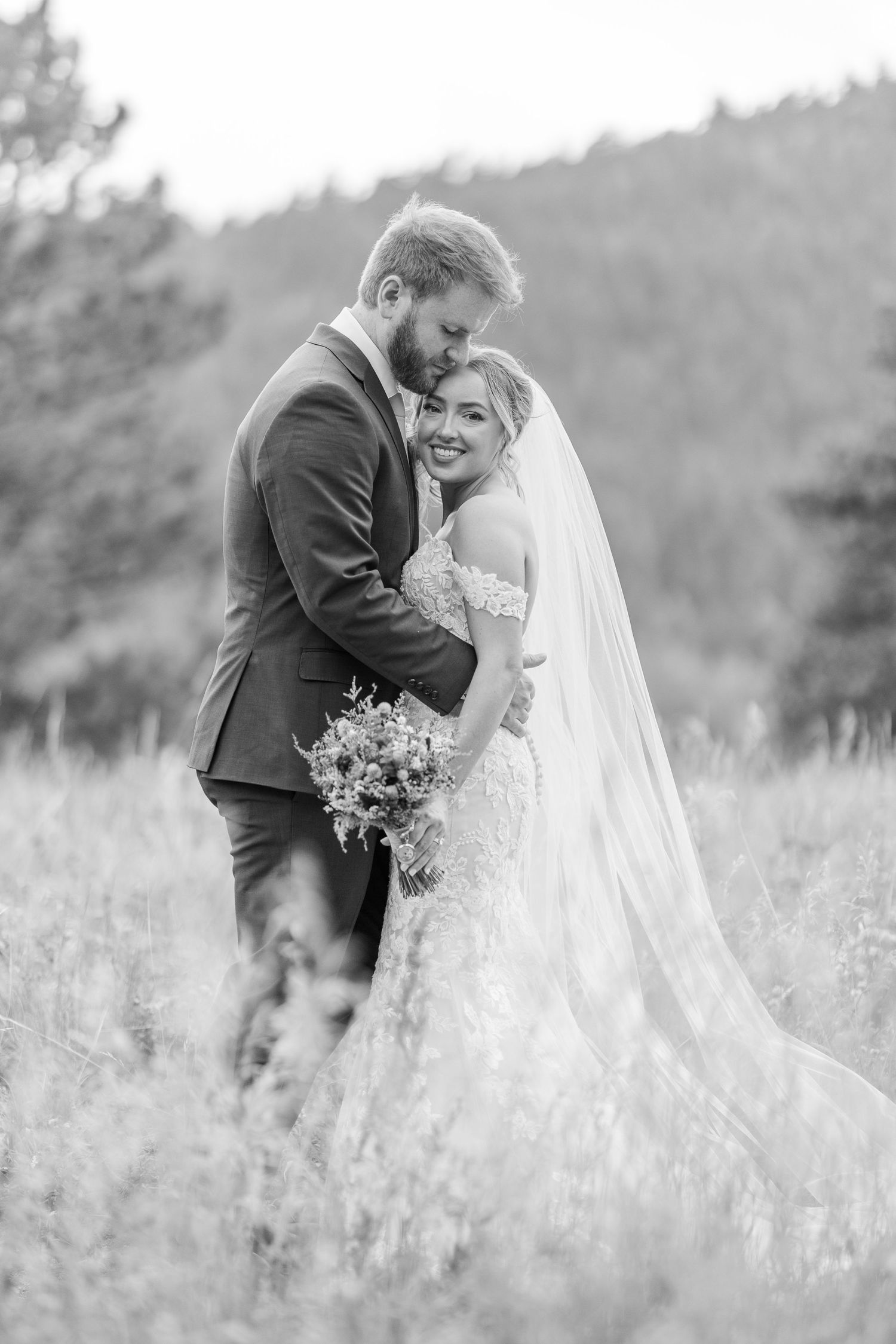 Black and white wedding photos show a romantic moment between newlyweds in a meadow of tall grass.