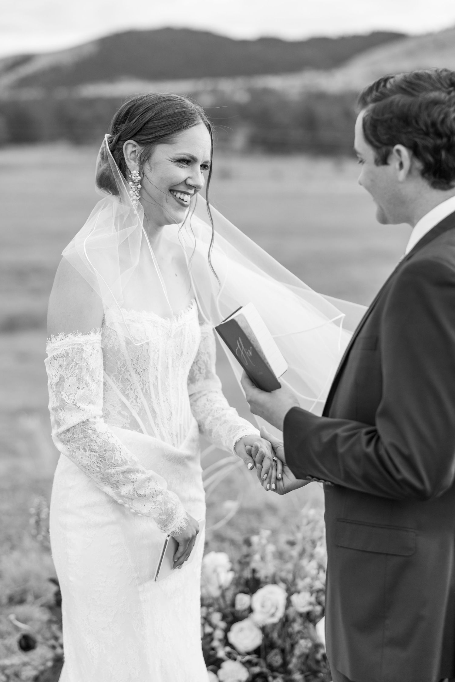 A wedding couple shares a joyful moment together in a scenic outdoor field during their ceremony.
