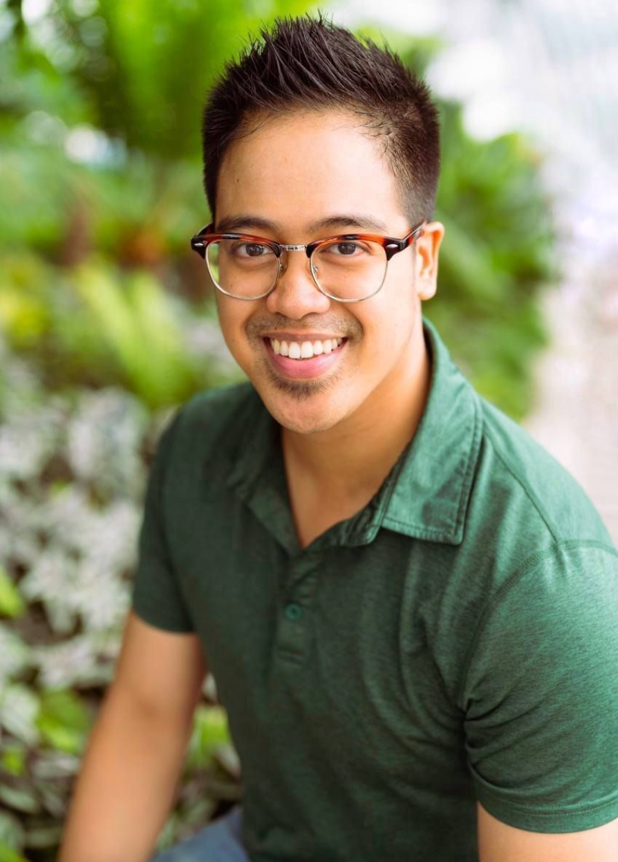 Smiling person wearing glasses and a green polo shirt photographed outdoors with greenery in the background.