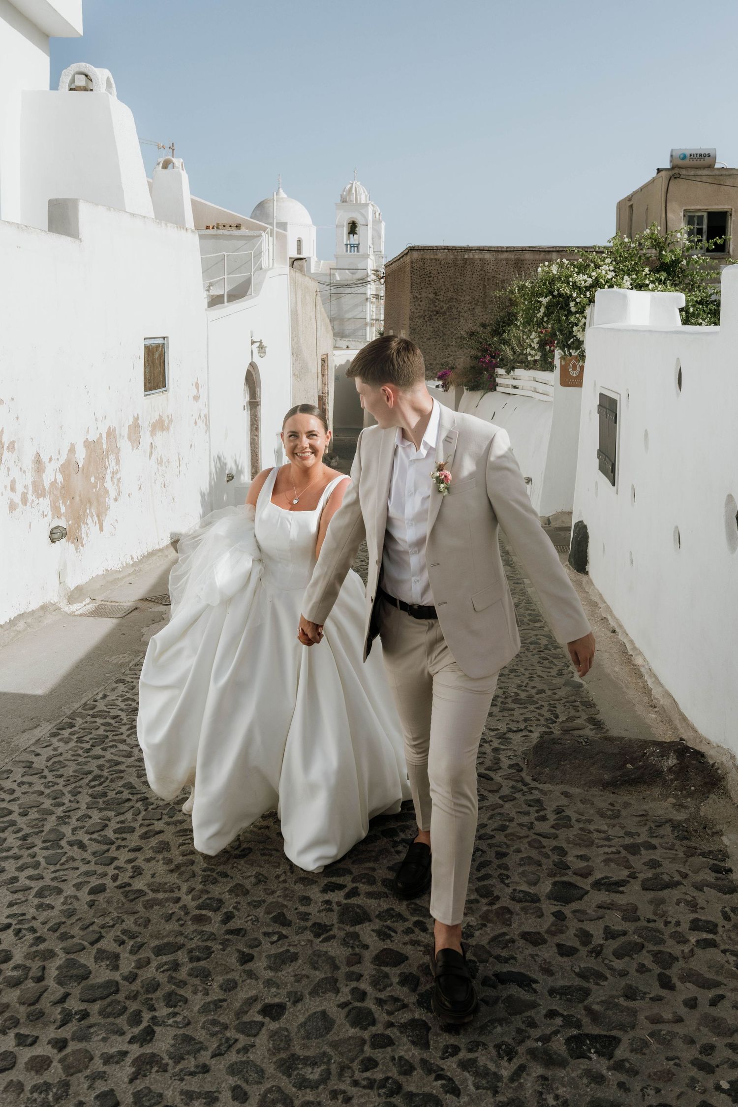 Bride and groom walking hand in hand through the streets of Santorini, captured by luxury wedding content creator Unveil by Hollie