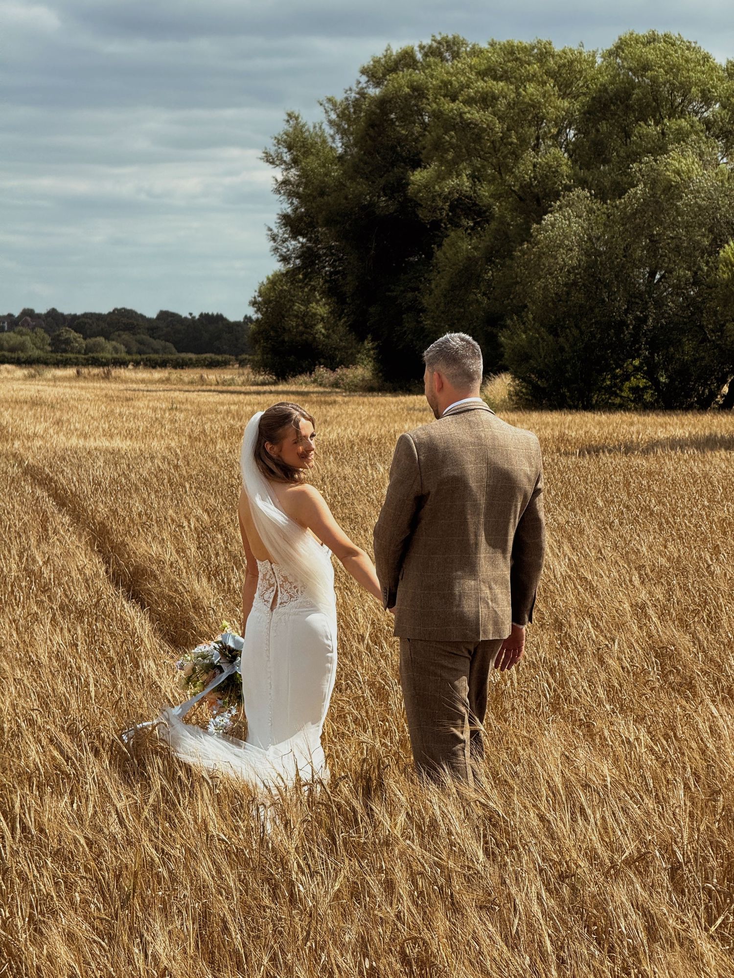 Bride and groom walking hand in hand through a golden countryside field on their wedding day, captured by luxury wedding content creator