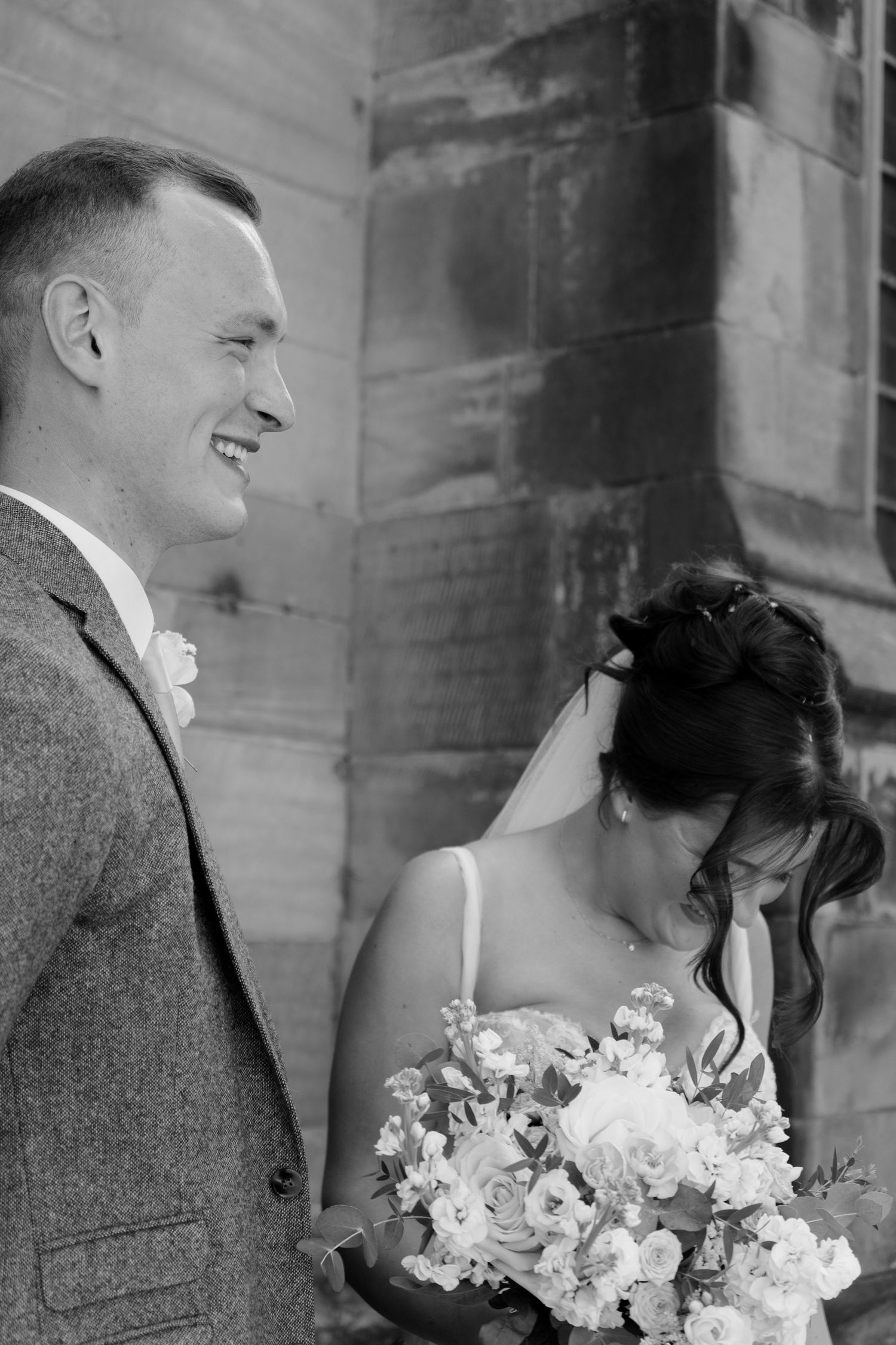Bride and groom sharing a candid wedding day moment outside their ceremony venue, captured in timeless black and white