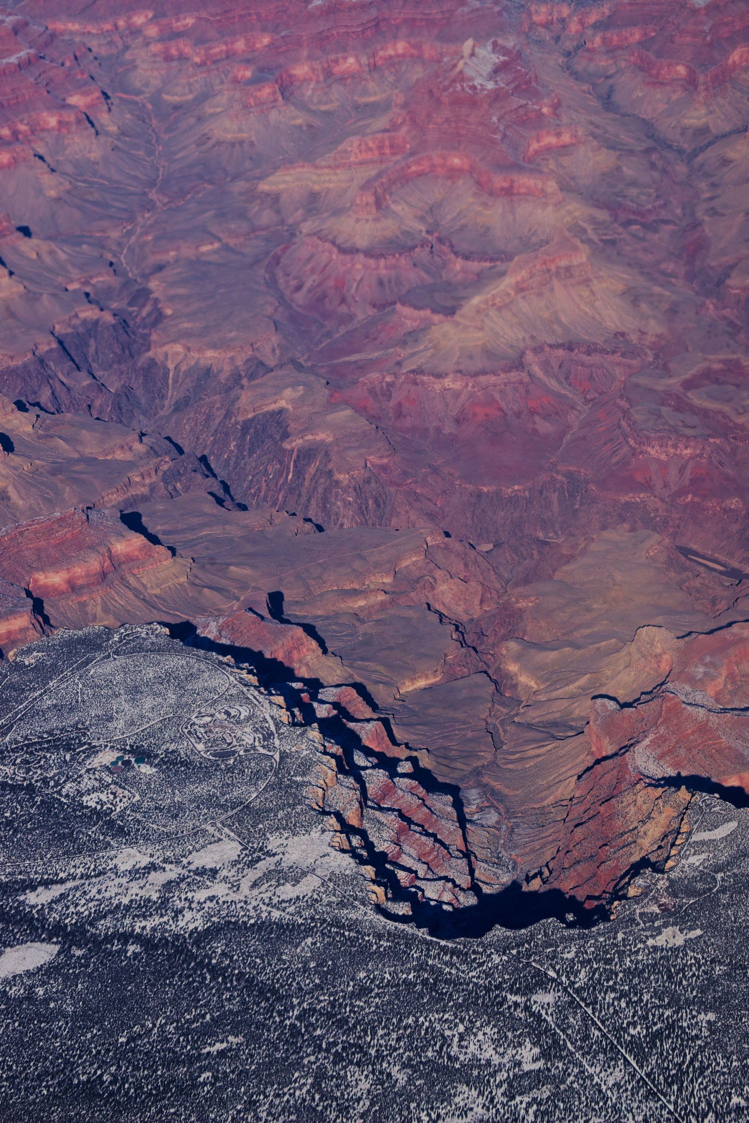 Aerial view of the Grand Canyon showcasing vibrant red rock layers, deep gorges, and snow-dusted terrain below.