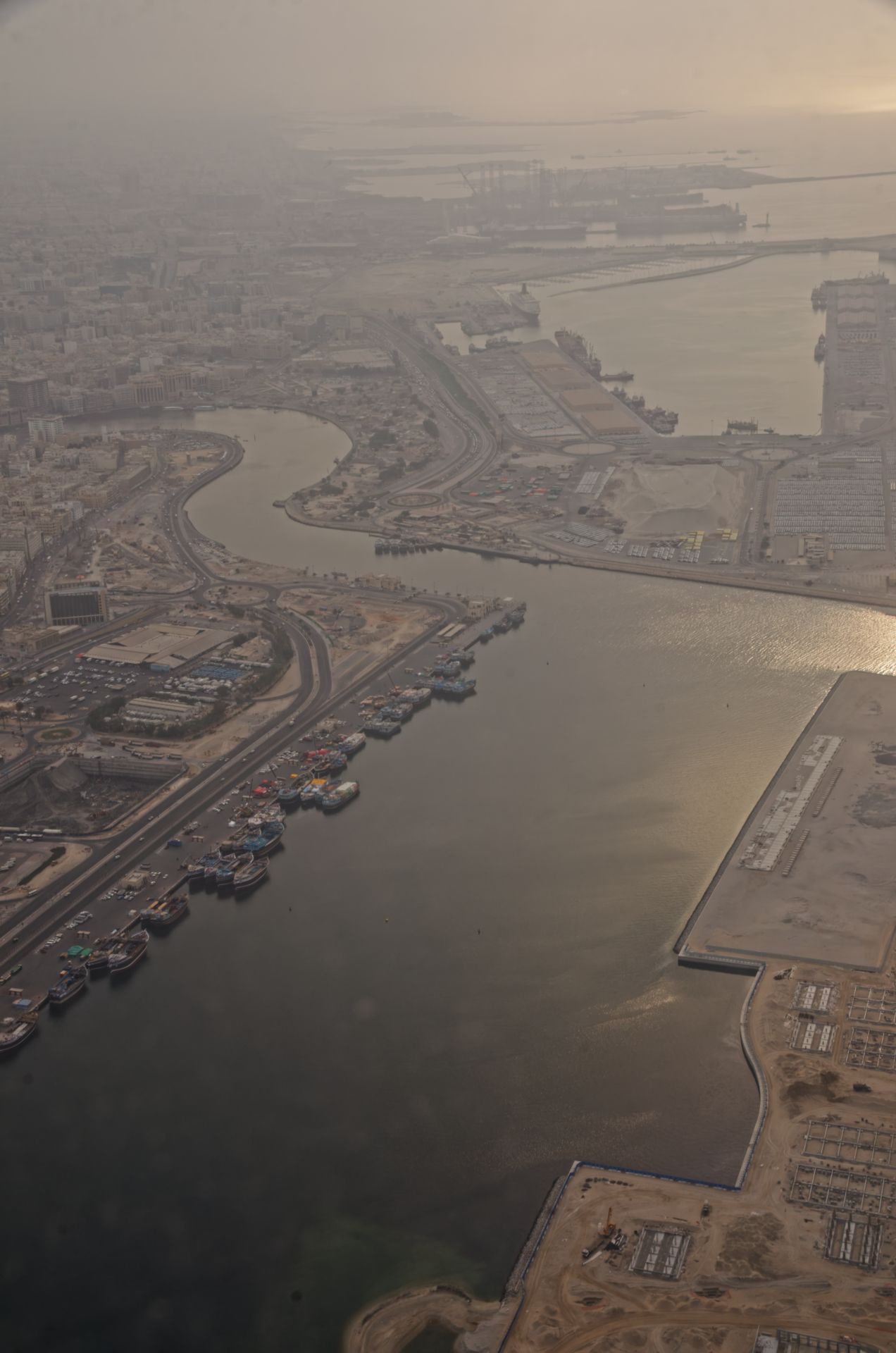 Aerial view of a coastal city harbor with docks, waterways, and urban infrastructure shrouded in hazy skies.