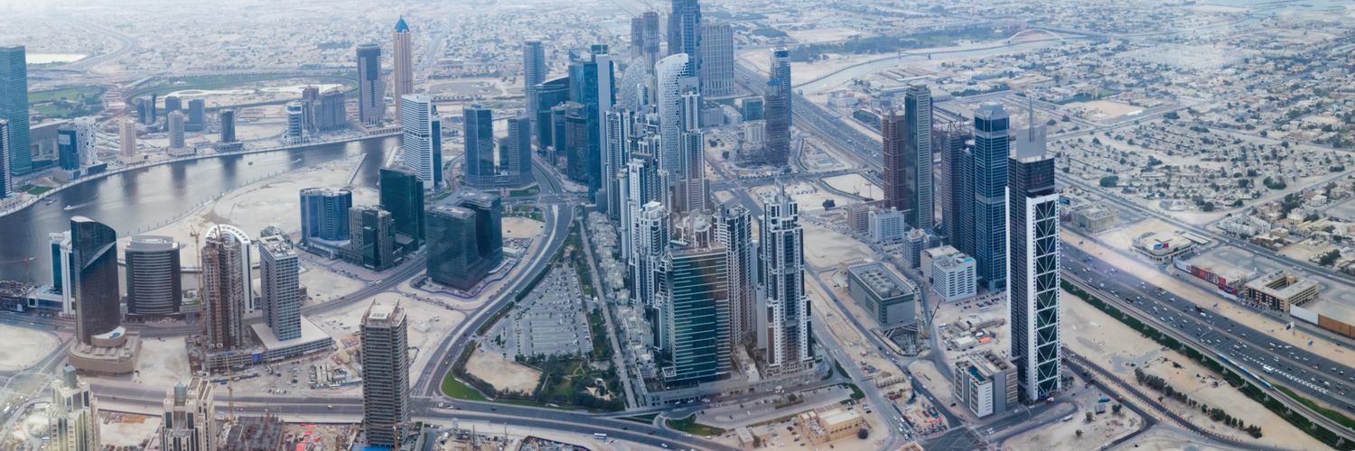 Aerial panoramic view of Dubai skyline with modern skyscrapers, highways, and urban infrastructure on a hazy day.