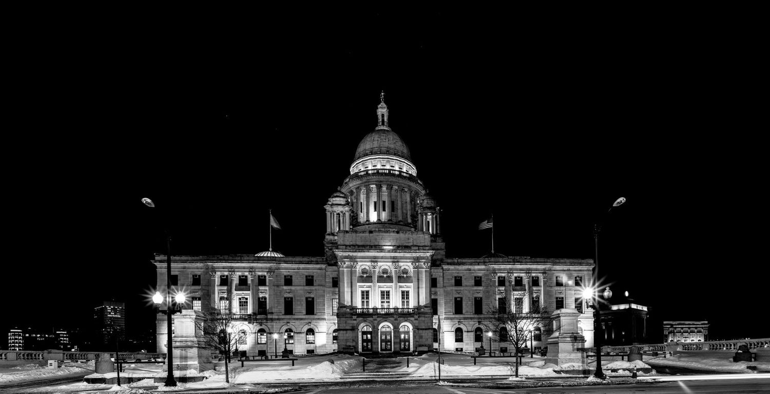 Black and white night photo of the Rhode Island State Capitol building illuminated against a dark sky.