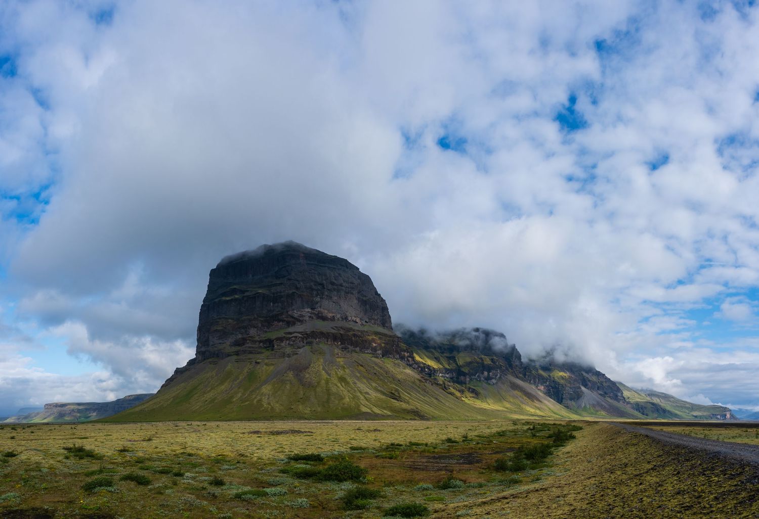 A dramatic volcanic rock formation rises under cloudy skies in Iceland's rugged landscape.