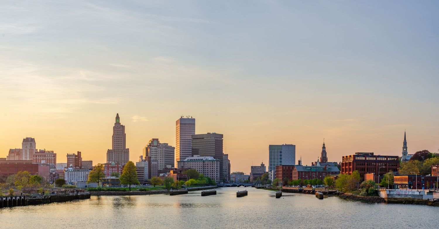 Providence Rhode Island skyline at sunset reflected in the calm river with city buildings and blue sky.