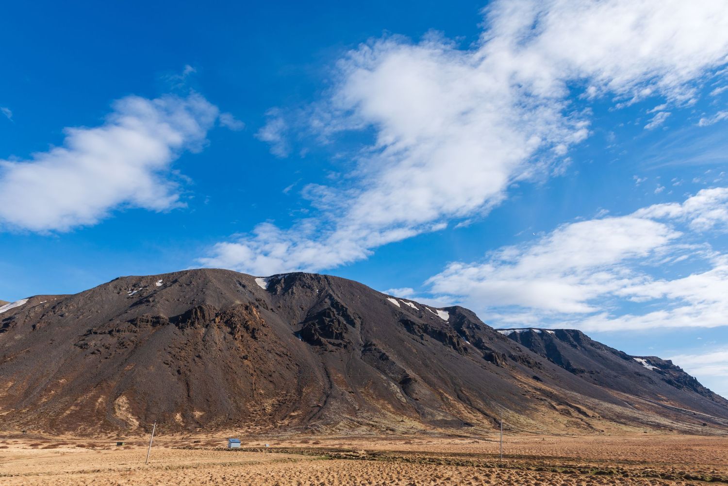 Barren volcanic mountain landscape under vivid blue sky with scattered clouds in Iceland's rugged terrain.