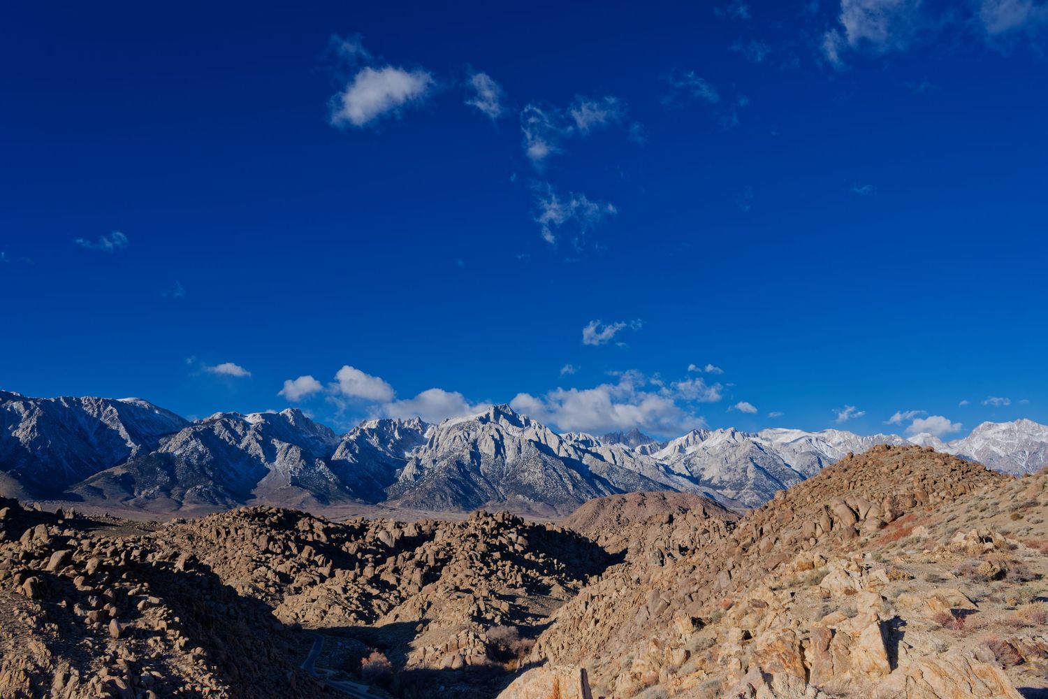 Snow-capped Sierra Nevada mountains rise above rocky Alabama Hills terrain under a vivid deep blue sky in California.