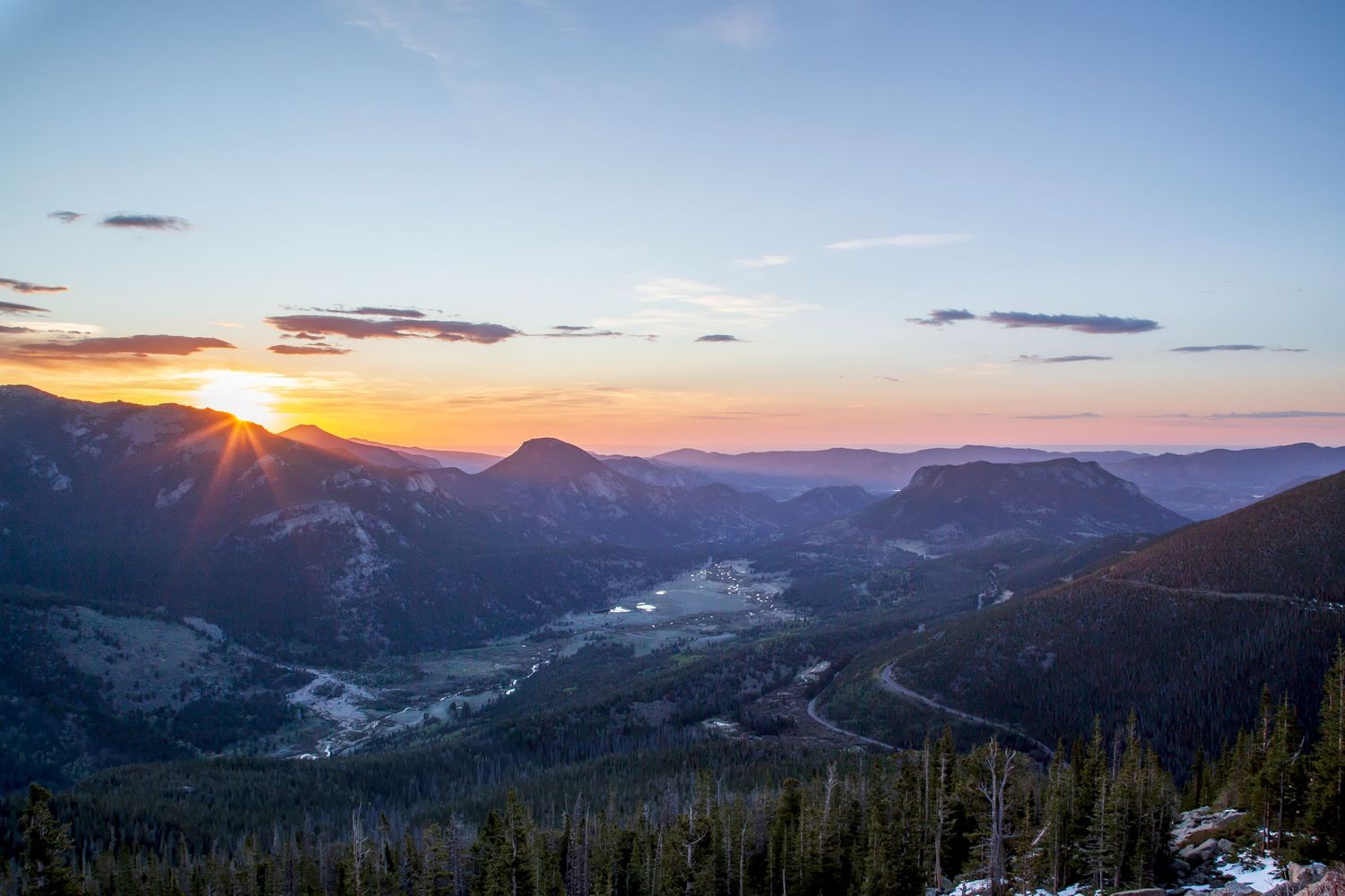 Stunning mountain sunset with orange sky over a forested valley and winding river in the Rocky Mountains.