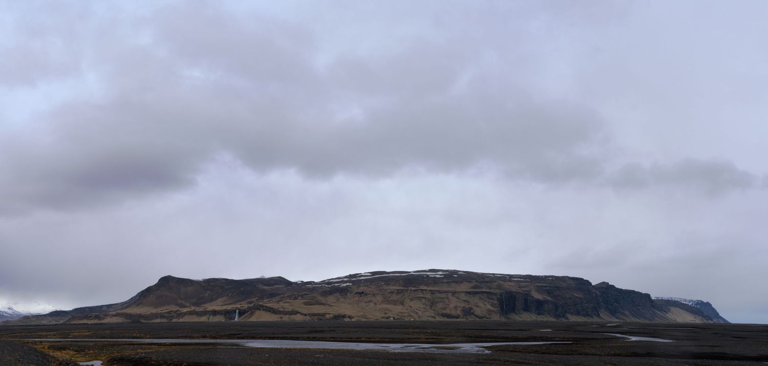 A dramatic Icelandic landscape featuring a flat-topped volcanic mountain under a moody overcast sky with dark plains below.