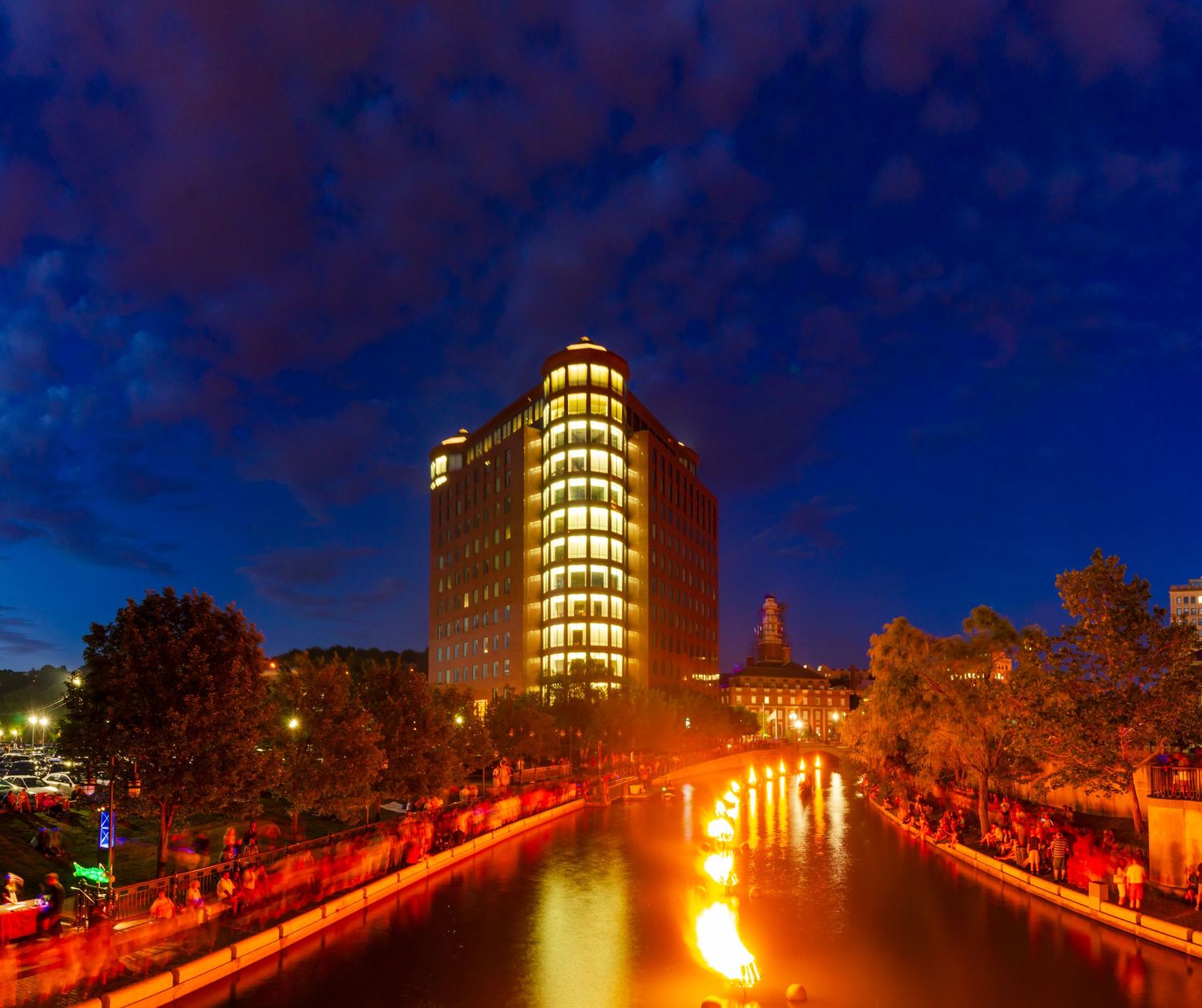 Providence skyline reflected in the river at night with colorful lights and dramatic blue sky.