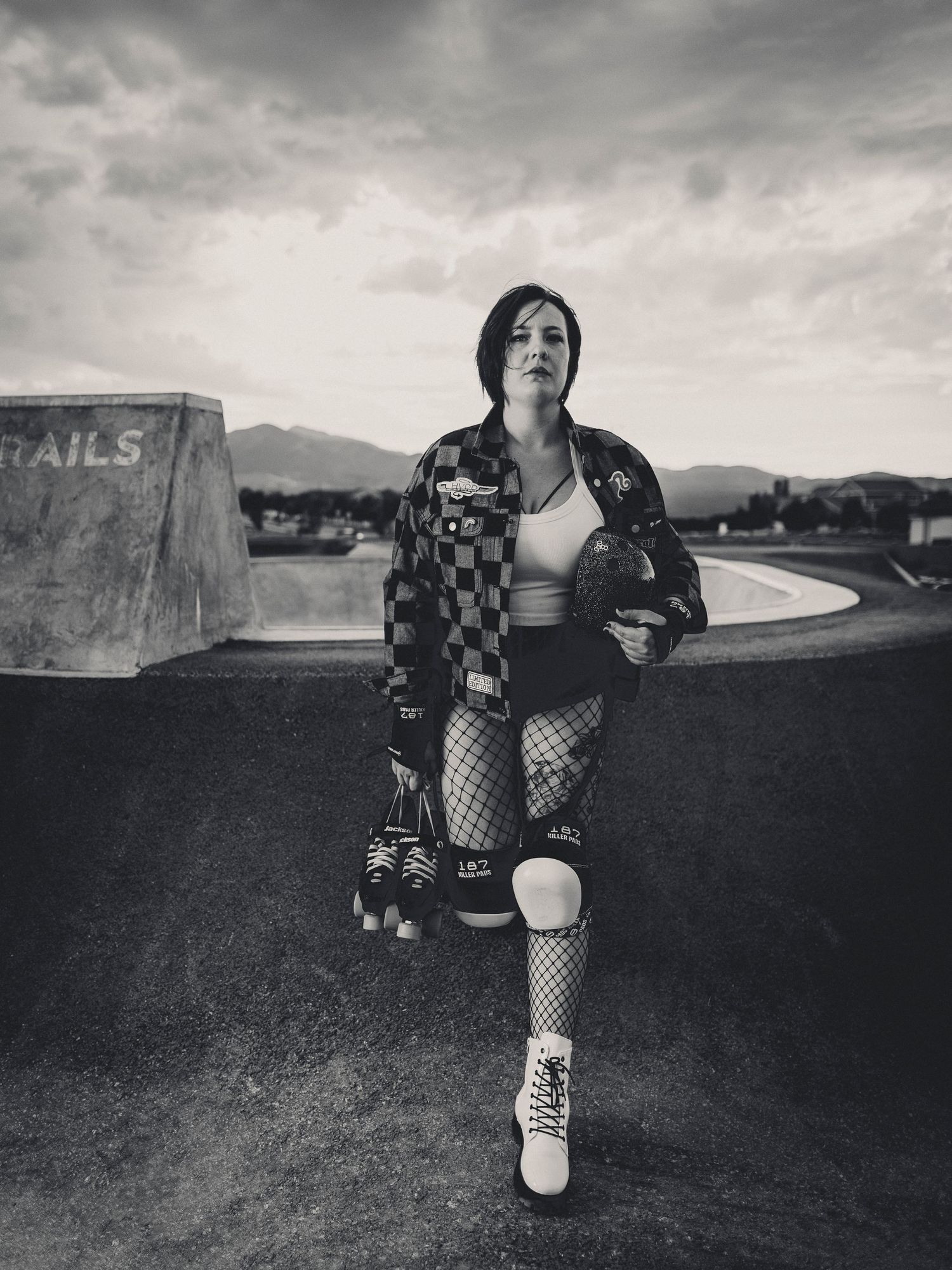 Black and white portrait of a woman in roller derby gear at an outdoor skate park.