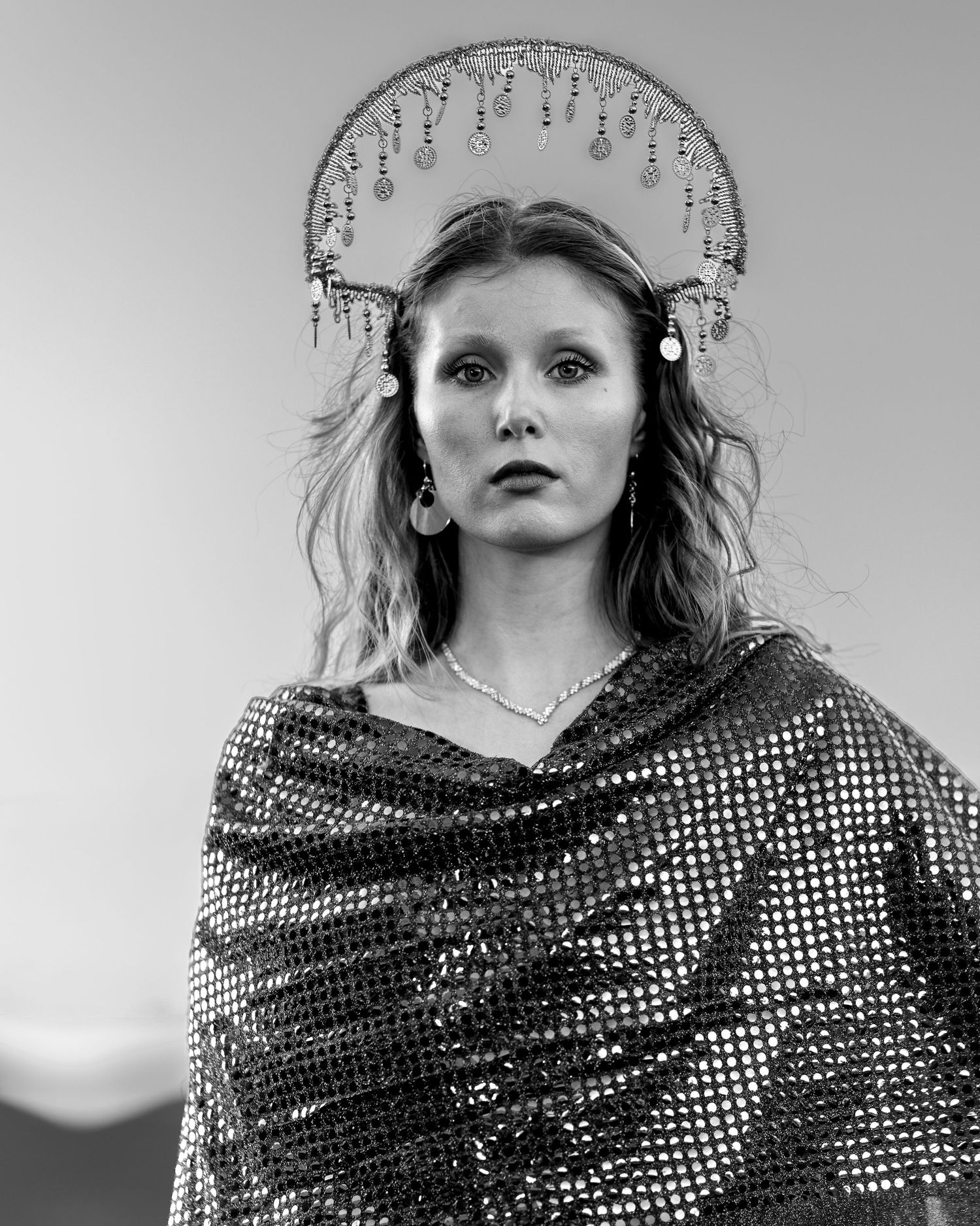 Black and white portrait of a woman wearing a decorative halo crown and sequined shawl.