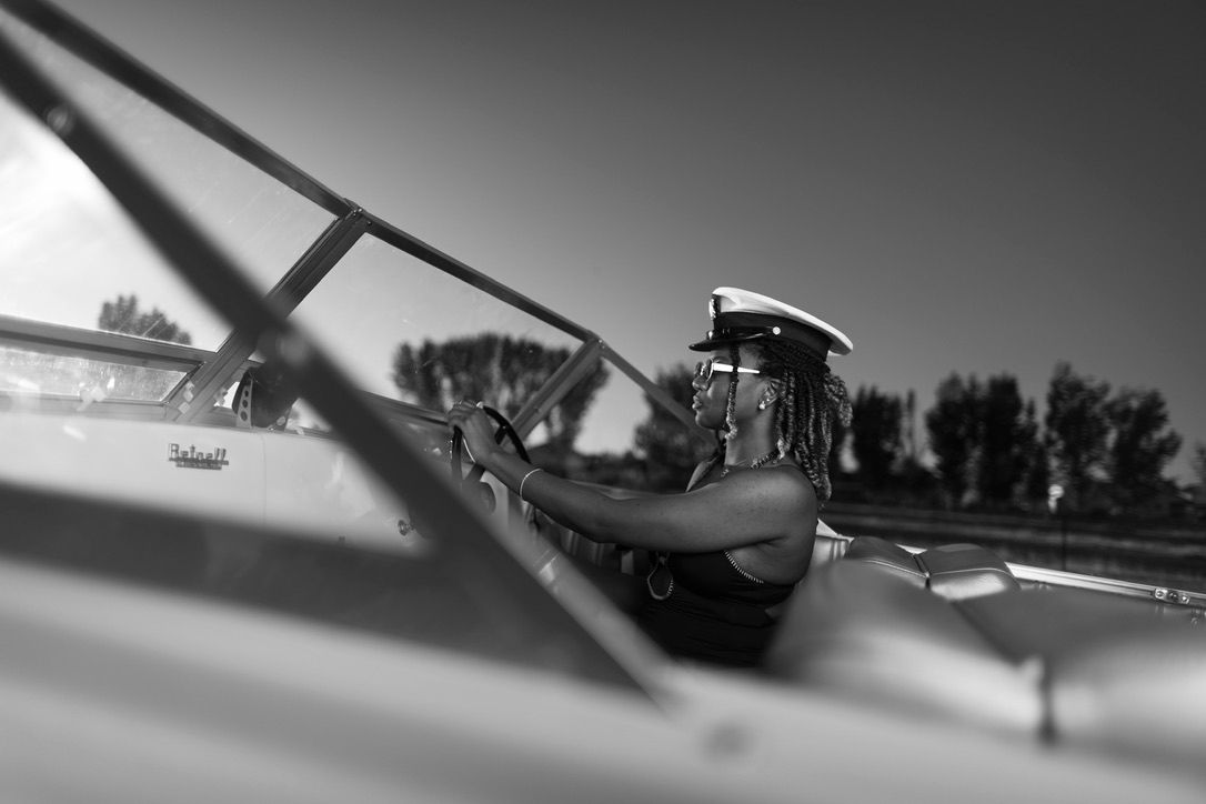 Black and white photo of a pilot in a vintage biplane cockpit on a sunny day.