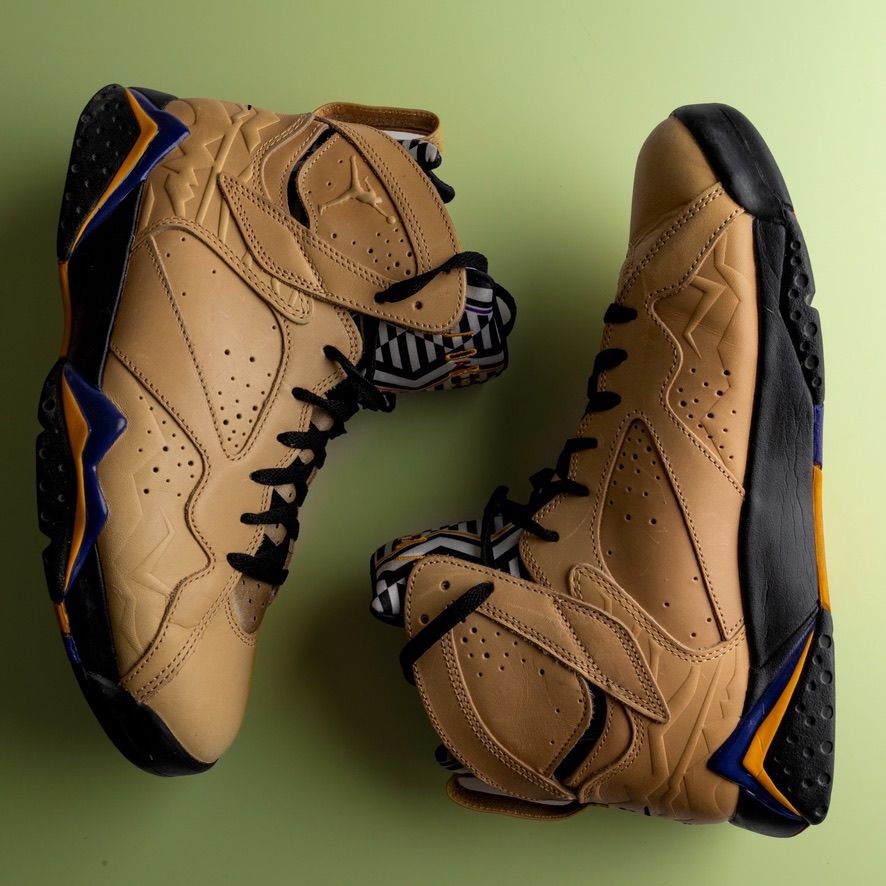 Pair of tan Air Jordan 7 retro basketball shoes with blue and black details on green background.