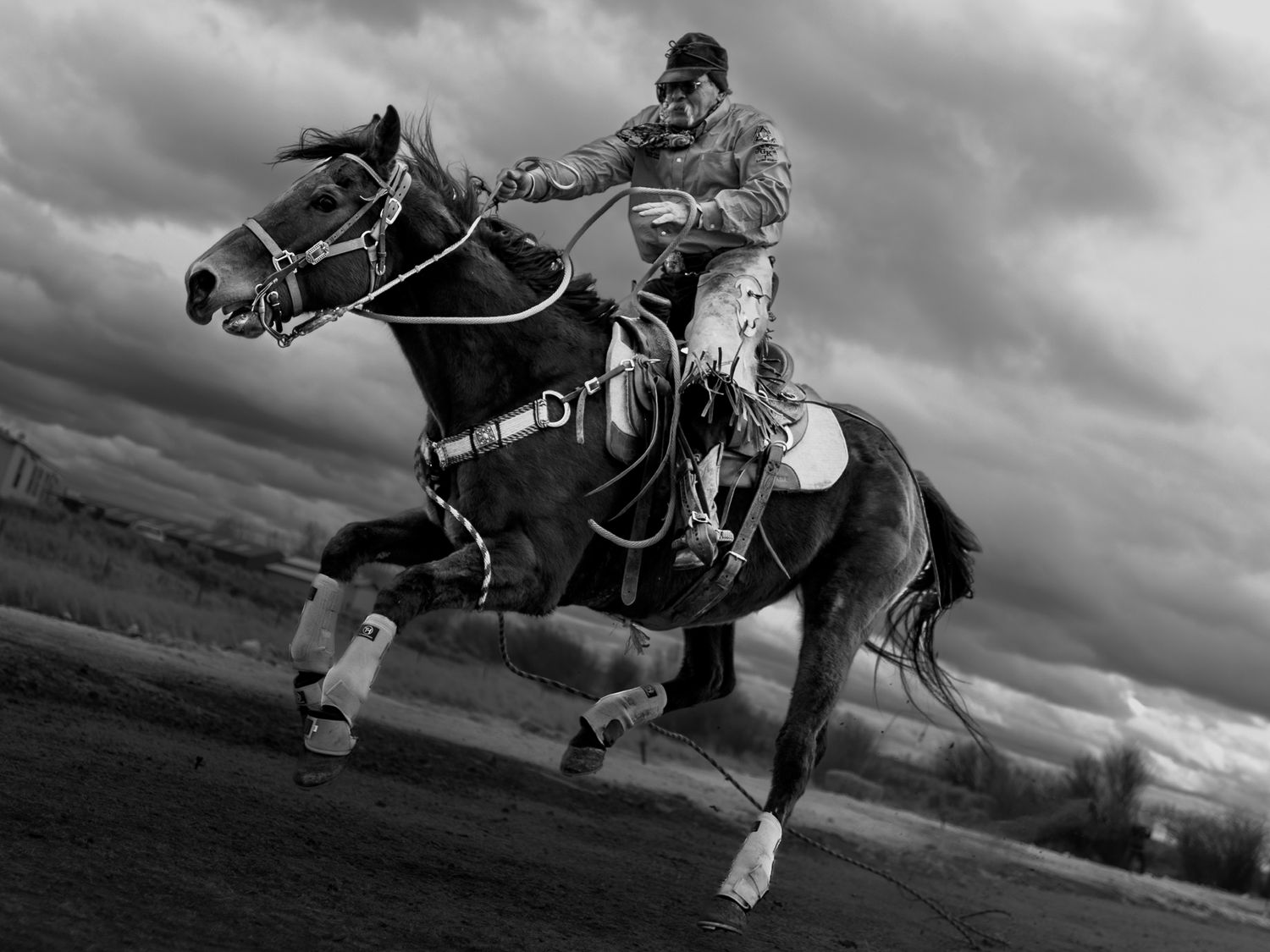 Black and white photo of a jockey riding a galloping horse under dramatic cloudy skies.