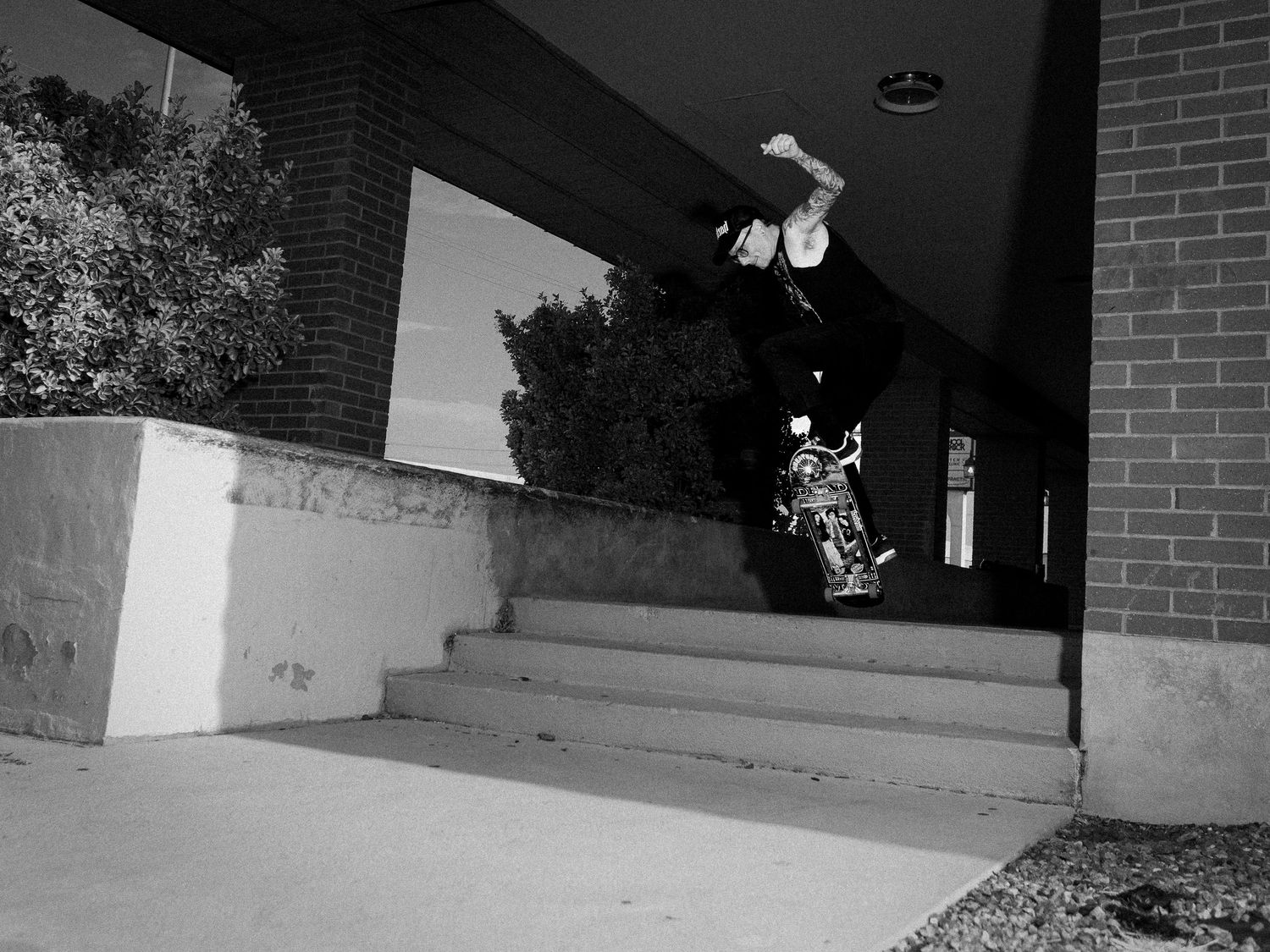 Skateboarder performing a wall ride trick on brick building steps in black and white urban skateboarding photo.