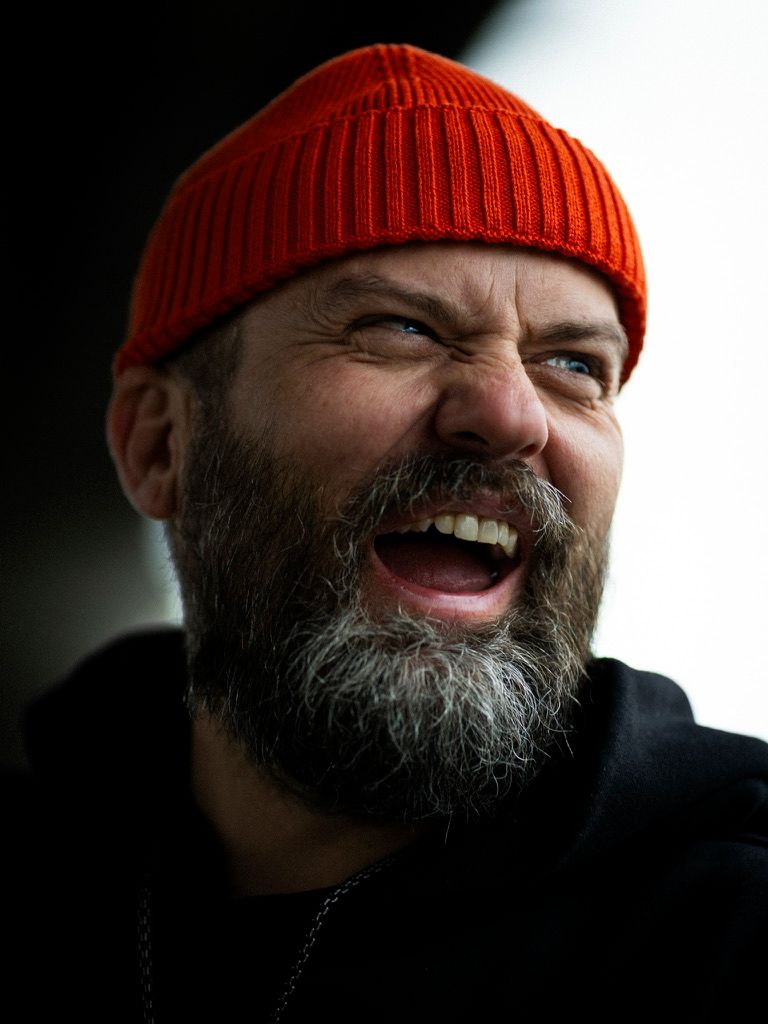 Bearded man in a red beanie hat laughing outdoors in a candid portrait photo.